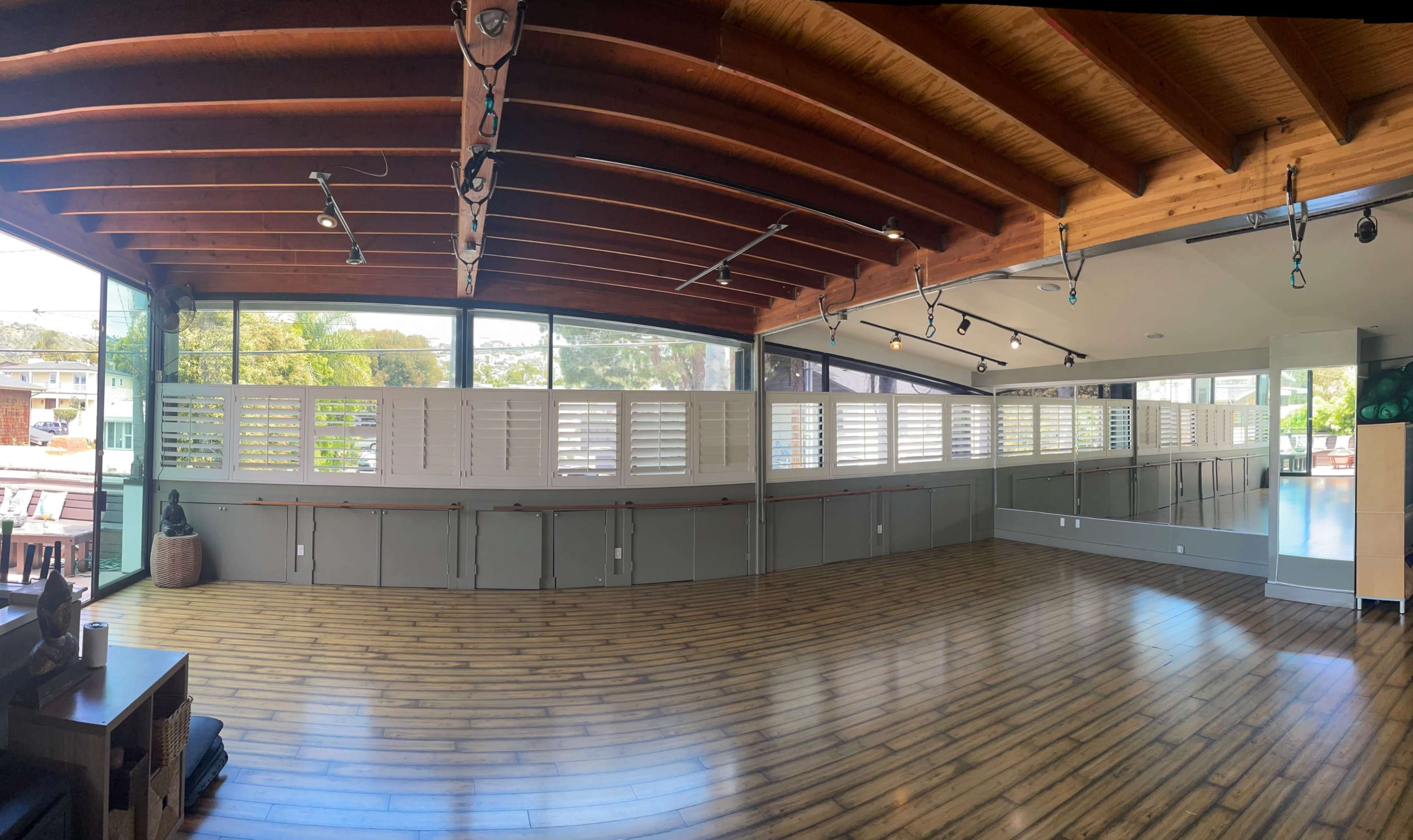 A spacious indoor area with wooden beams on the ceiling, large windows, and a wooden floor, featuring partitioned walls with shutters.