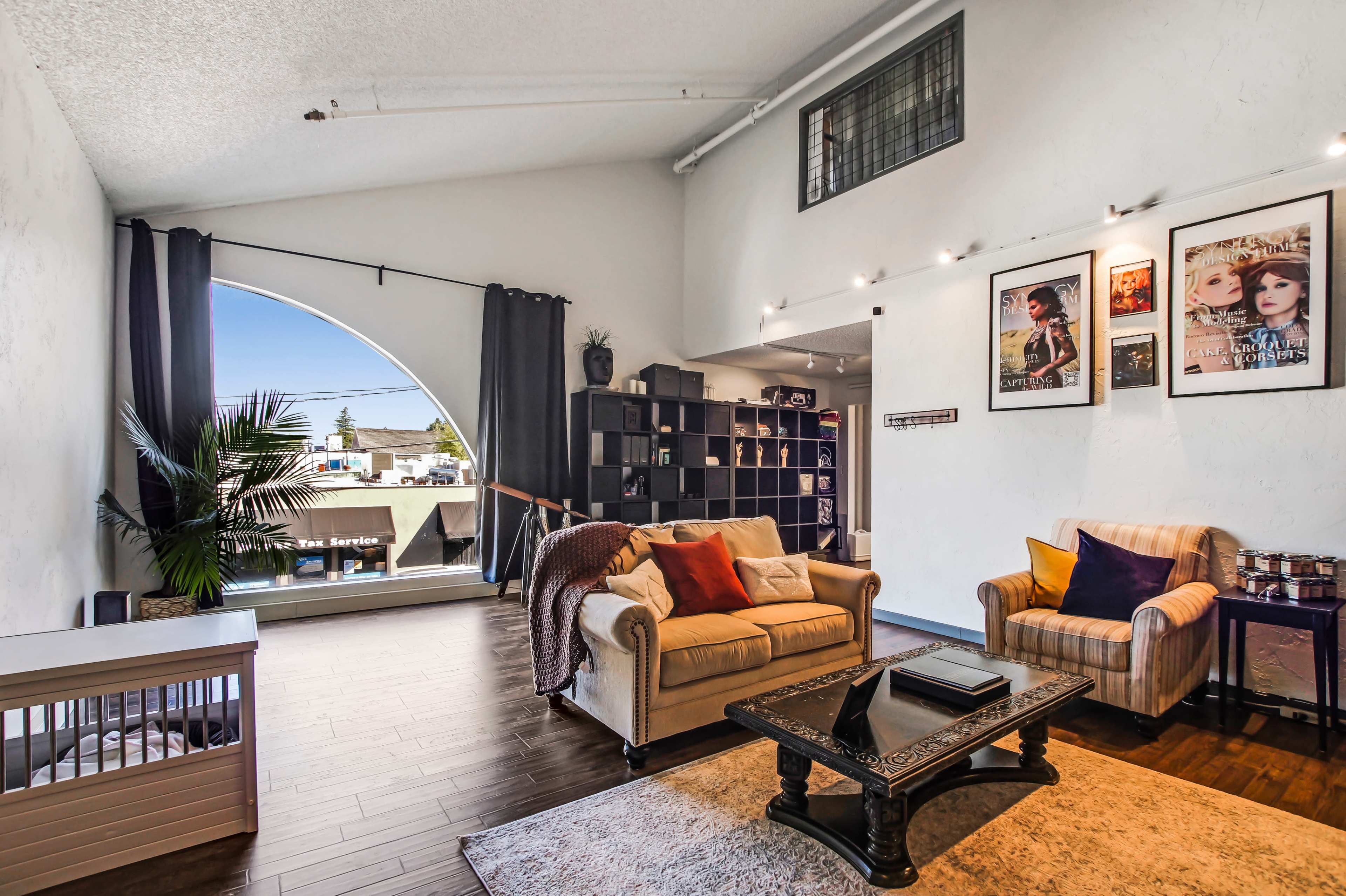 A modern living room with a large arched window, a comfortable seating area with a sofa and armchair, and framed artworks on the walls.