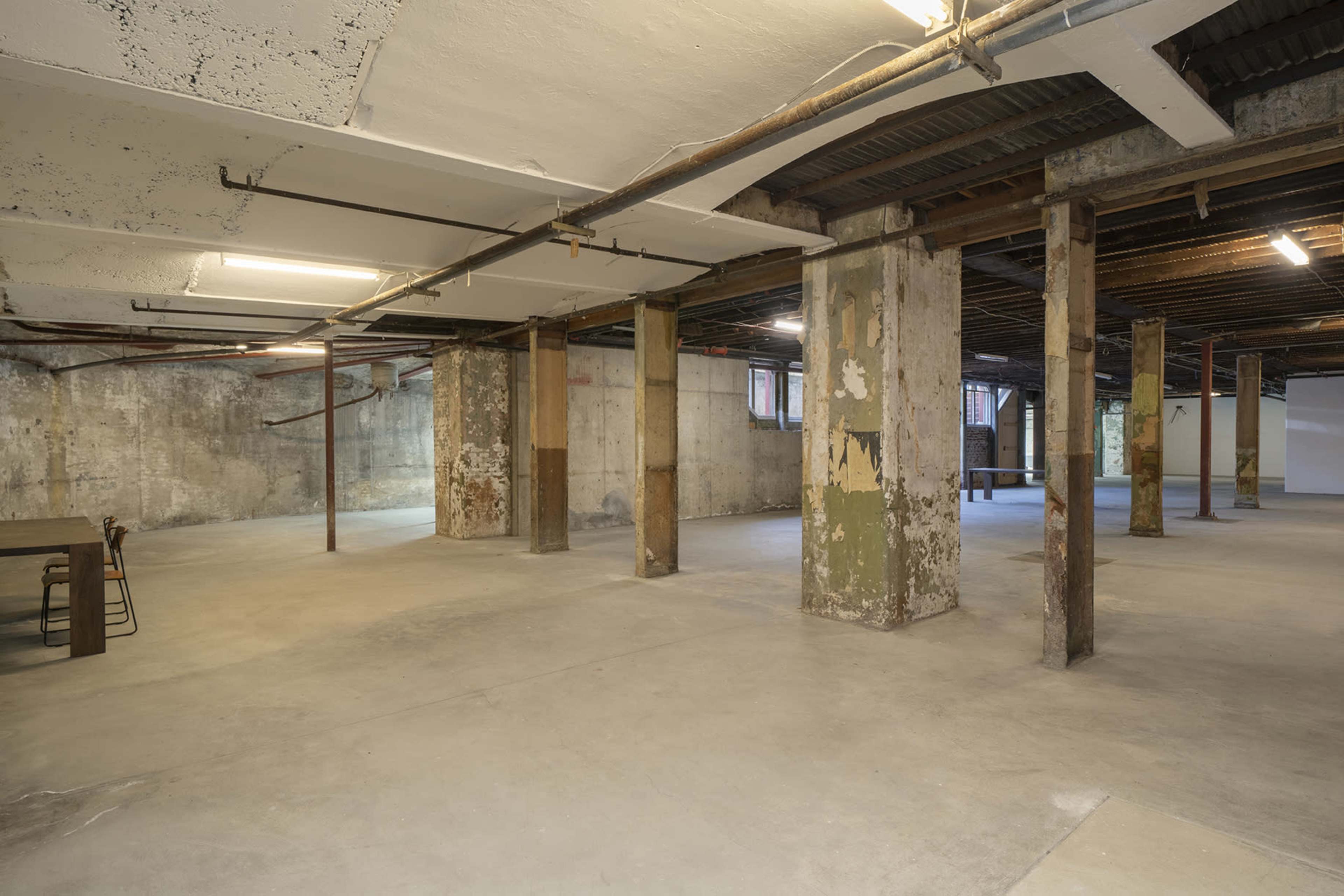 A spacious, unfinished basement with exposed concrete walls, ceiling beams, and several supporting columns.