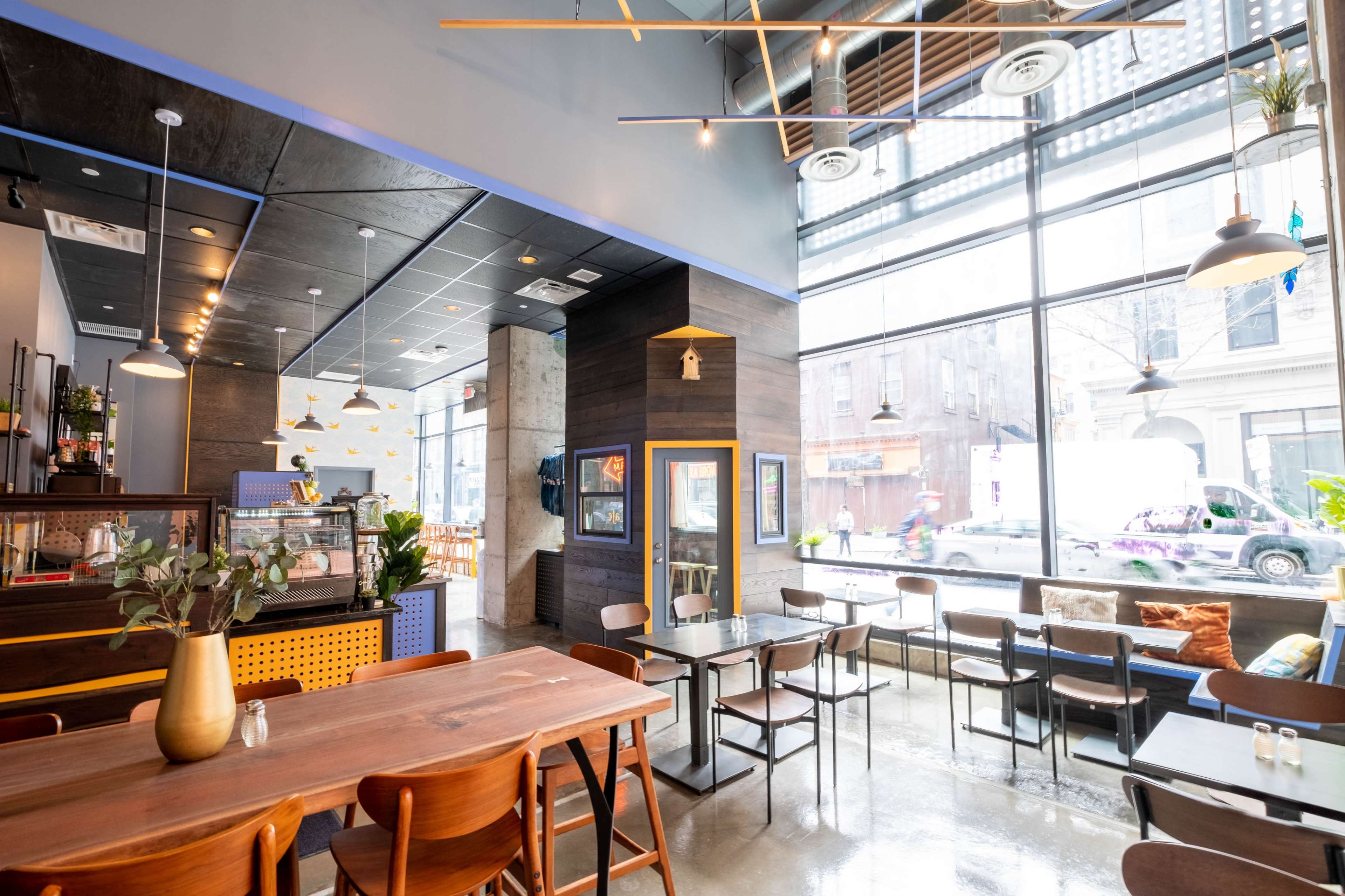 A modern café features large windows, wooden tables, and a sleek interior design with a view of the street outside.