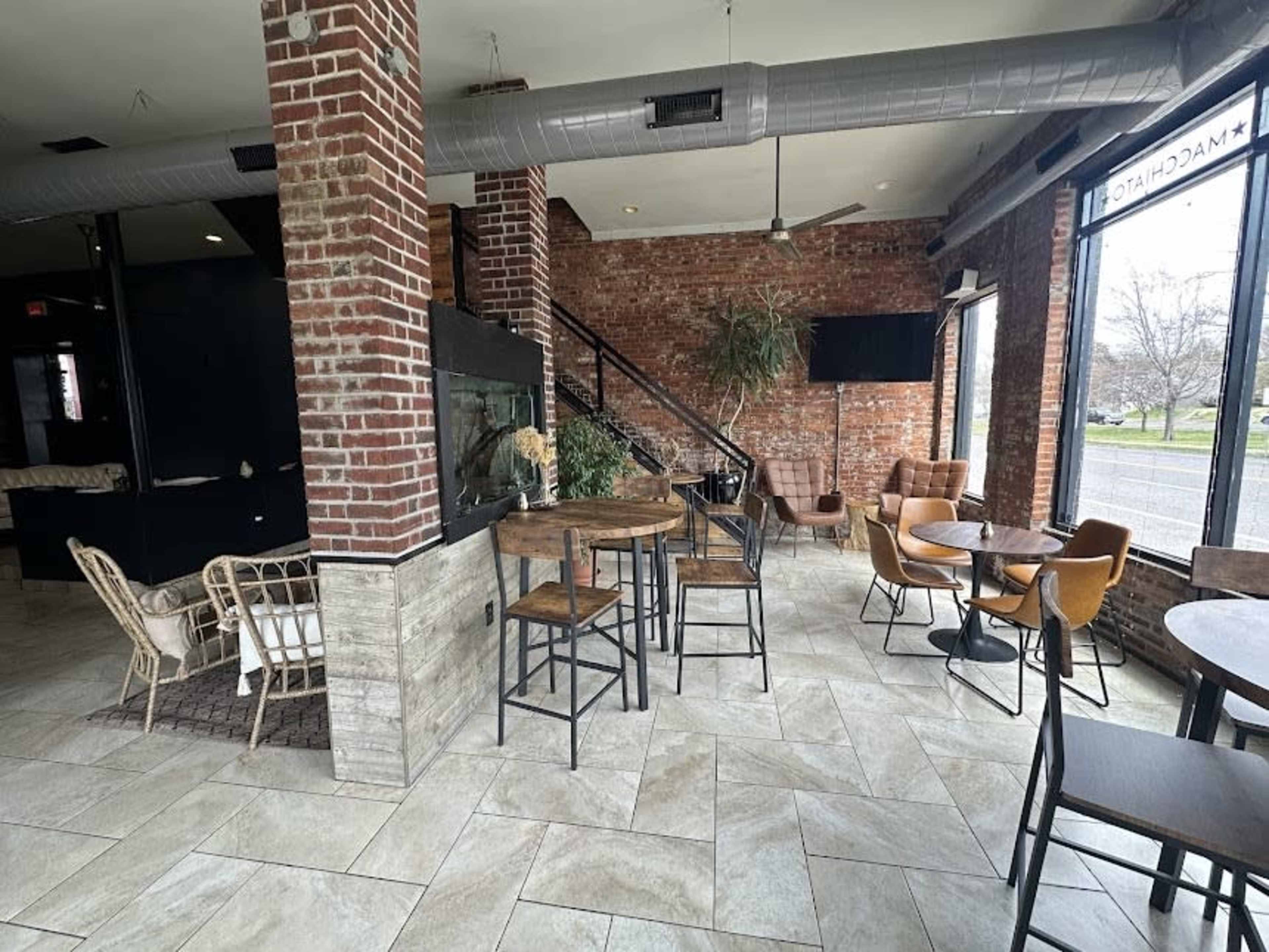 The image shows a modern restaurant interior with exposed brick walls, wooden furniture, and a seating area featuring tables and chairs near a staircase.