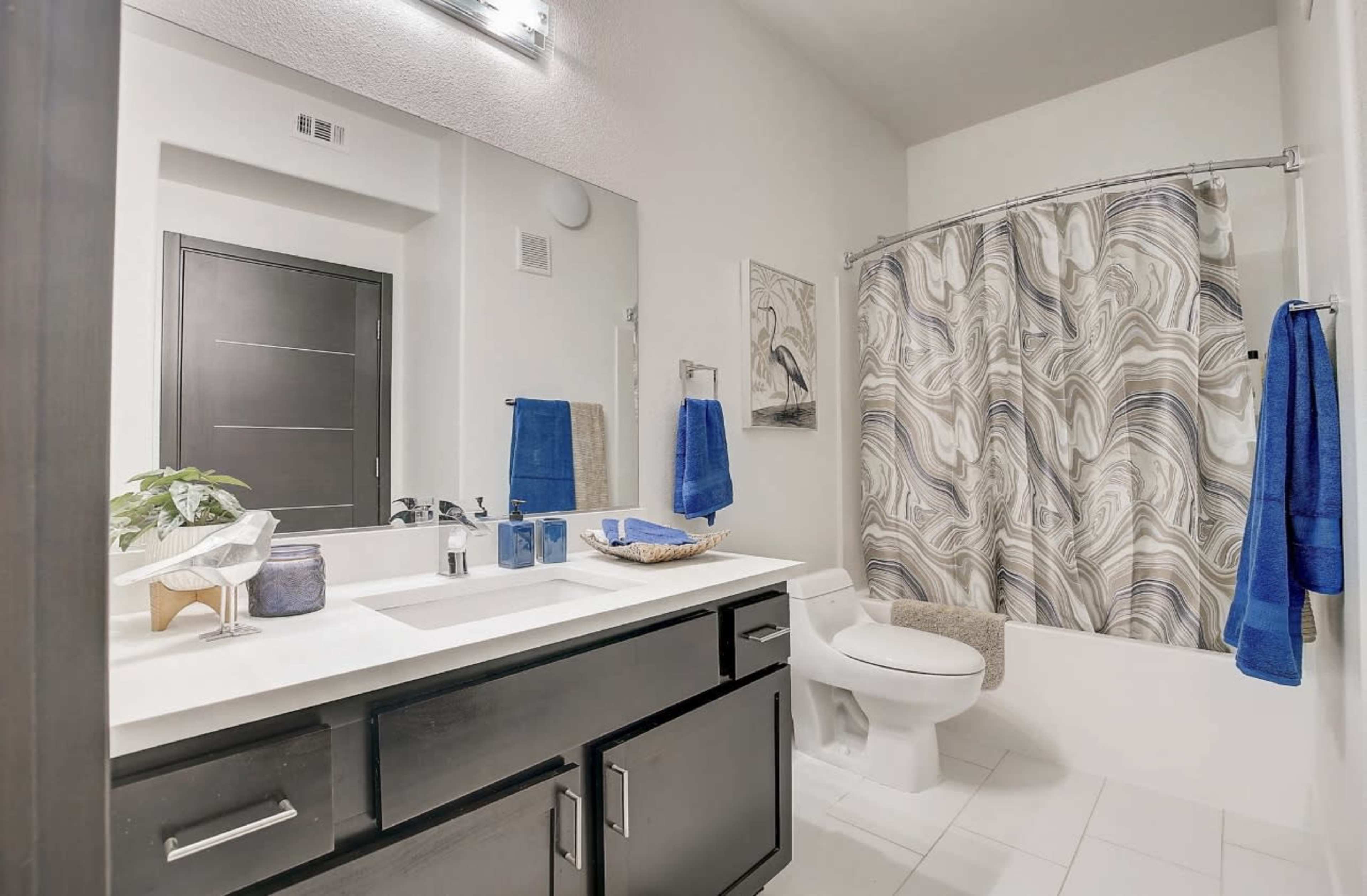 A modern bathroom featuring a white countertop with a sink, a shower with a patterned curtain, and dark cabinetry.