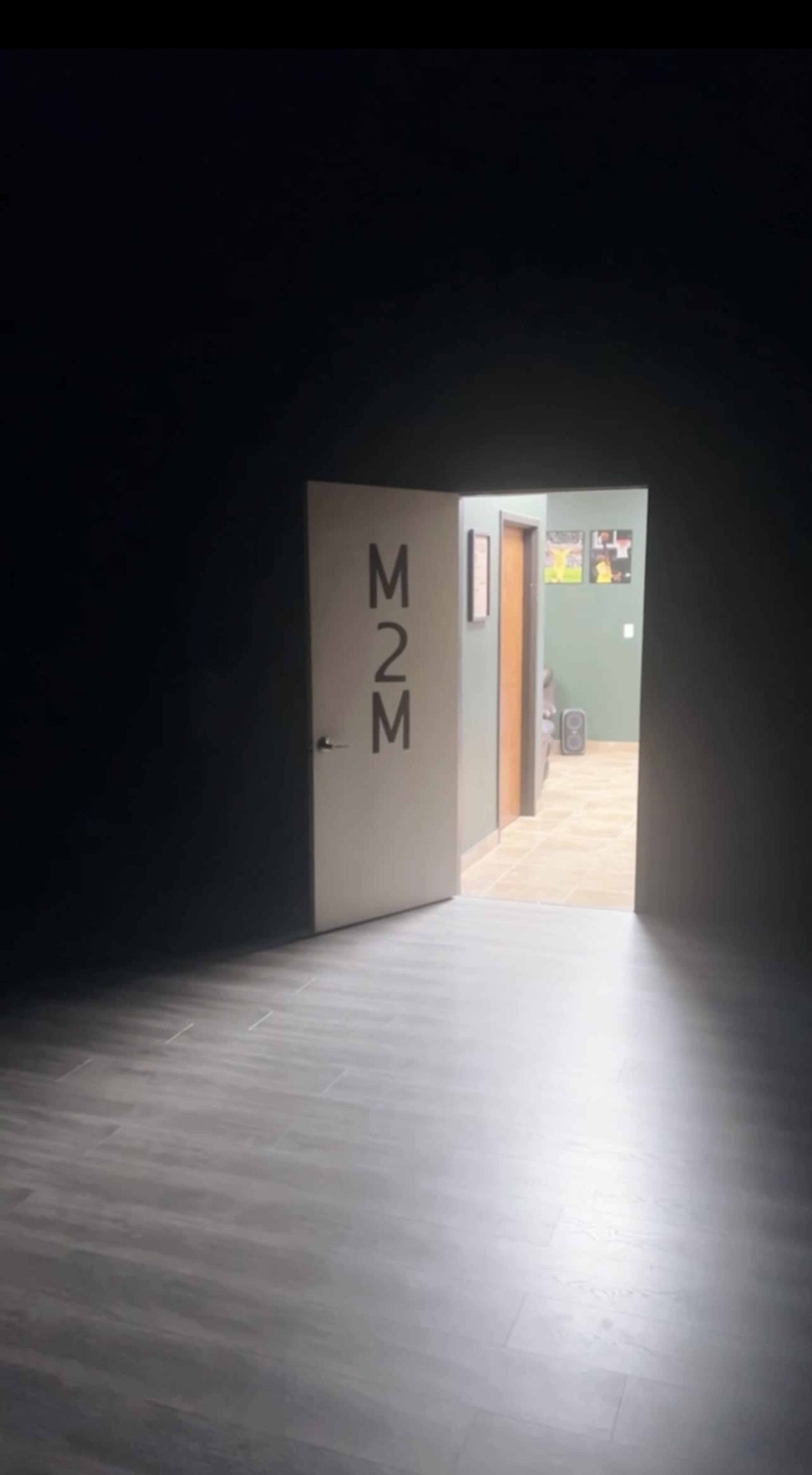 A partially open door with "M2M" written on it reveals a well-lit room in the background.