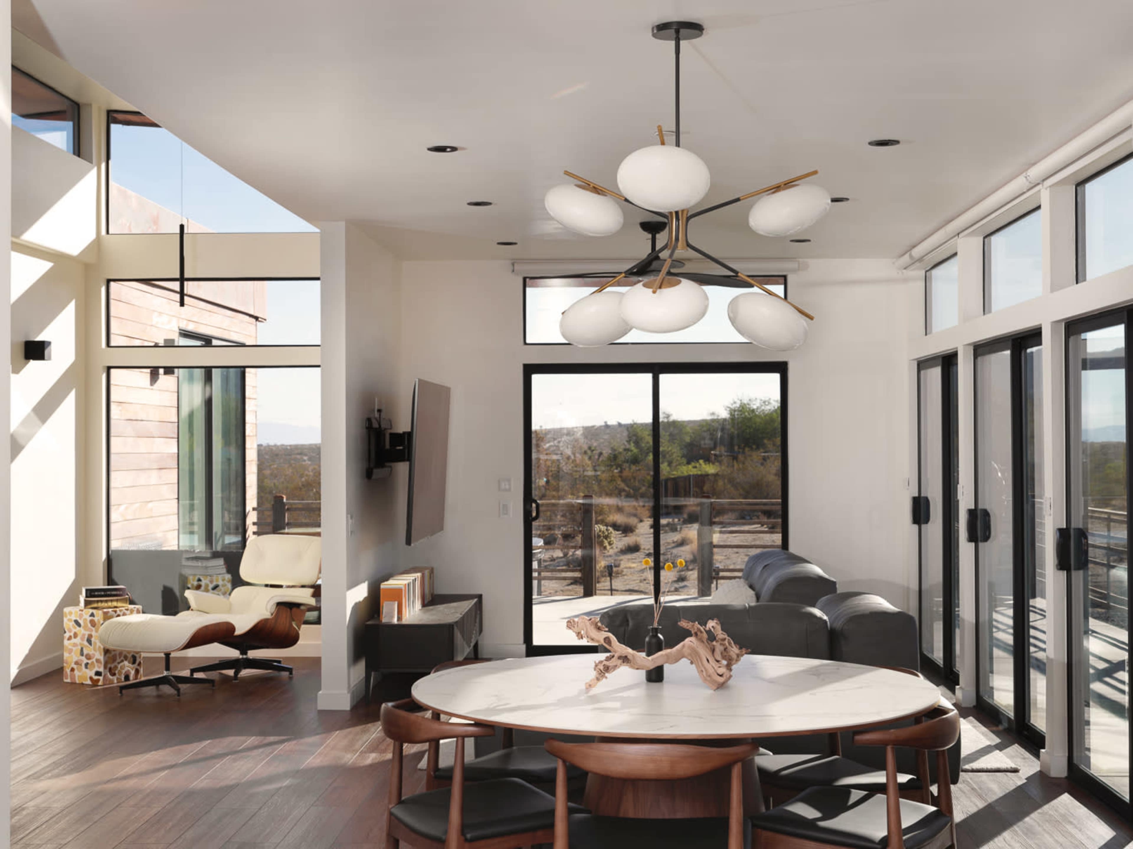 The image shows a modern living space with large windows, a circular dining table, and a unique light fixture hanging from the ceiling.