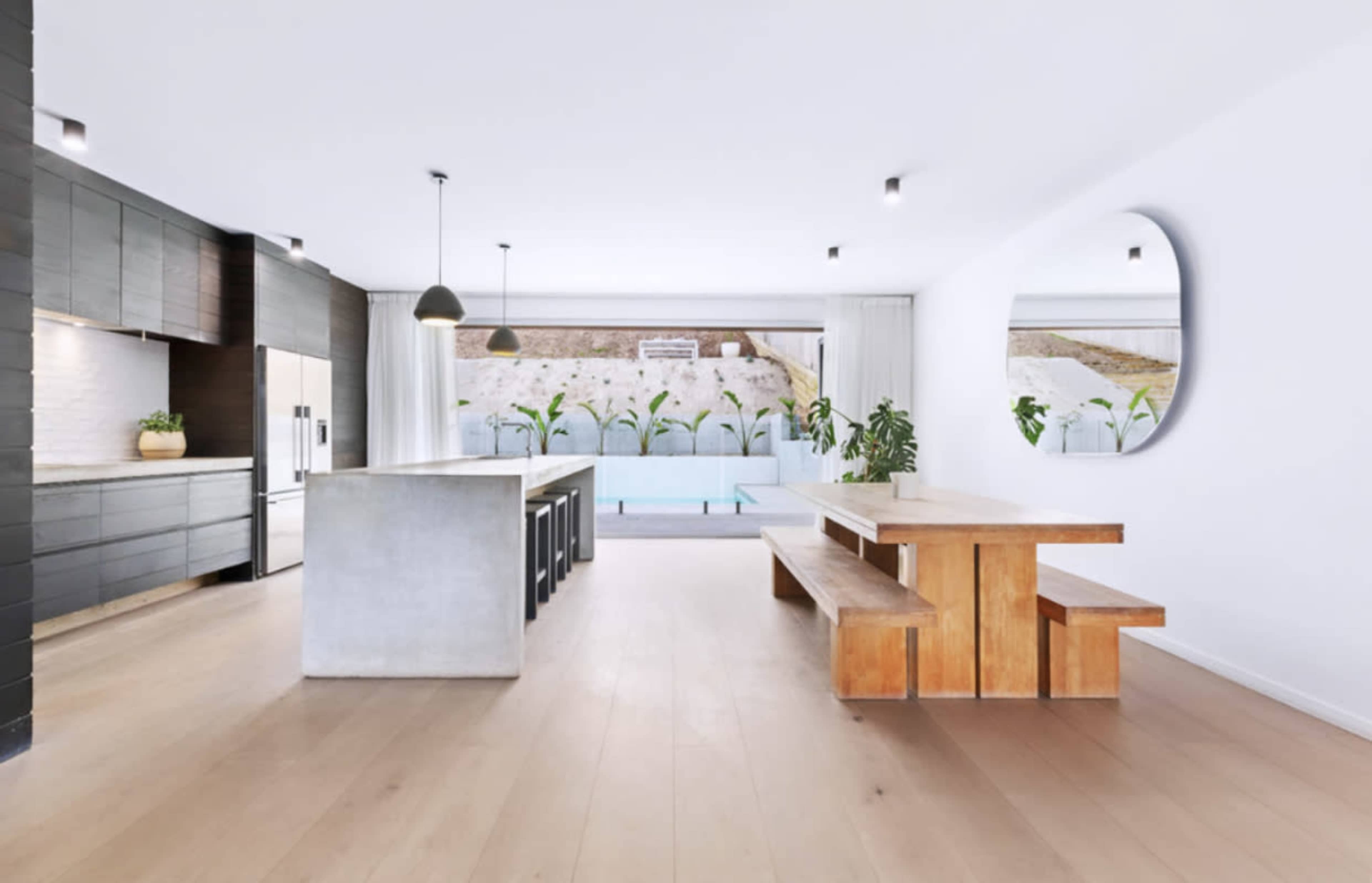 A modern kitchen and dining area with an island, wooden table, and large windows overlooking a patio.