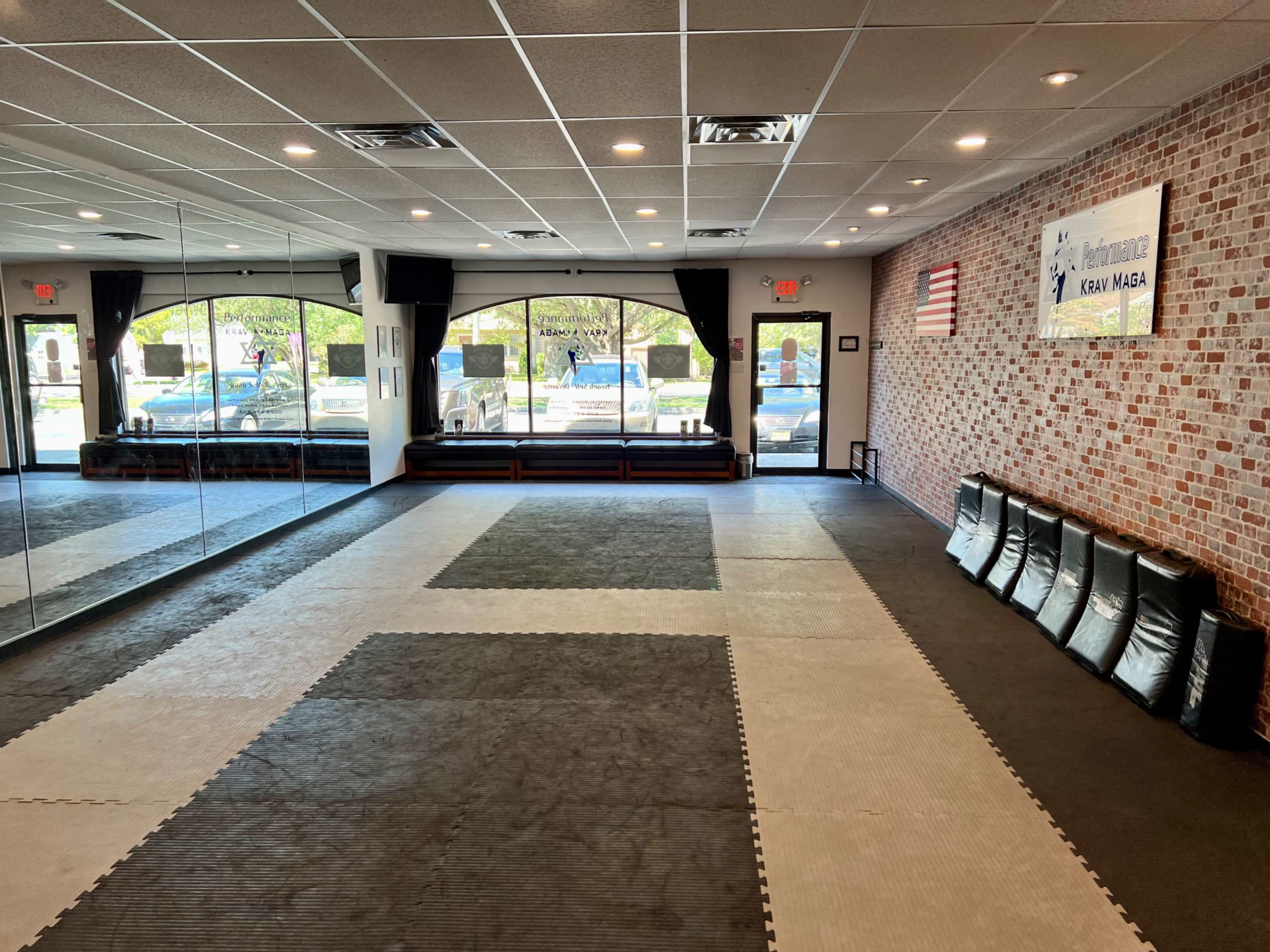 An empty martial arts training studio with mirrors on one wall and padded mats on the floor.