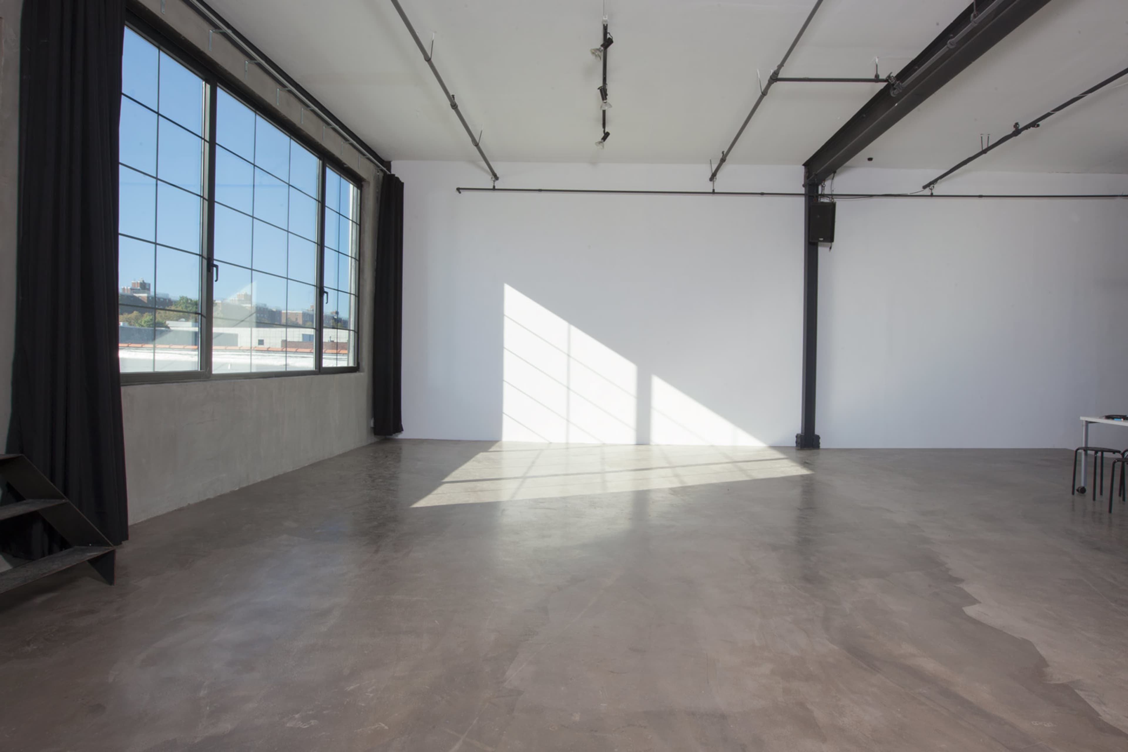 A spacious, empty room with concrete flooring and large windows that cast a diagonal shadow on the wall.