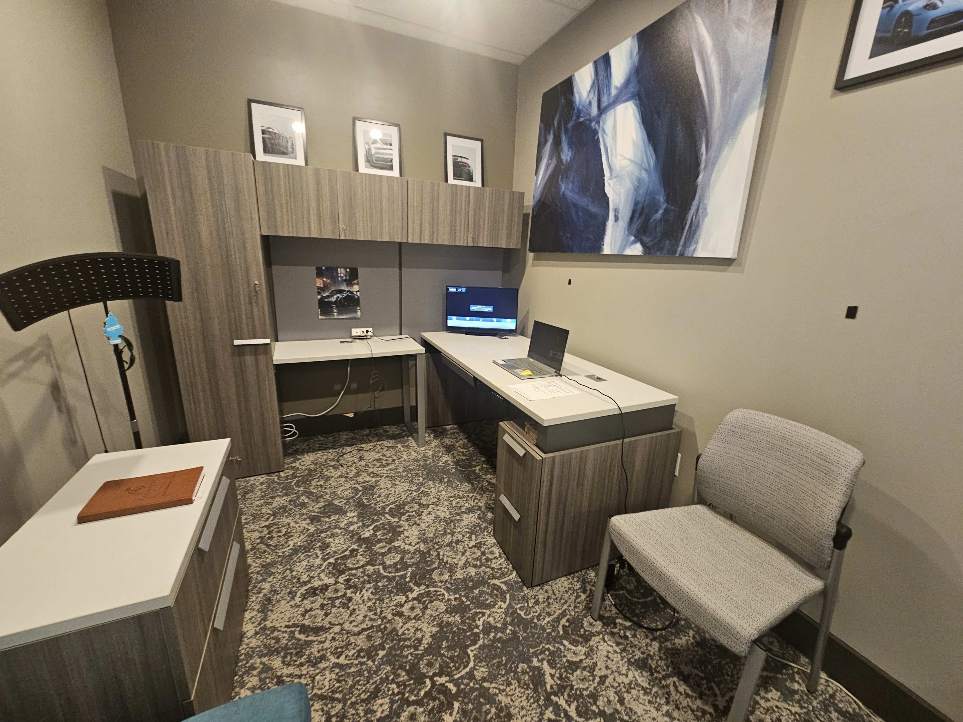 The image shows a modern office workspace featuring a desk with a computer, a wall-mounted display, and minimalist furniture against a neutral-colored wall.