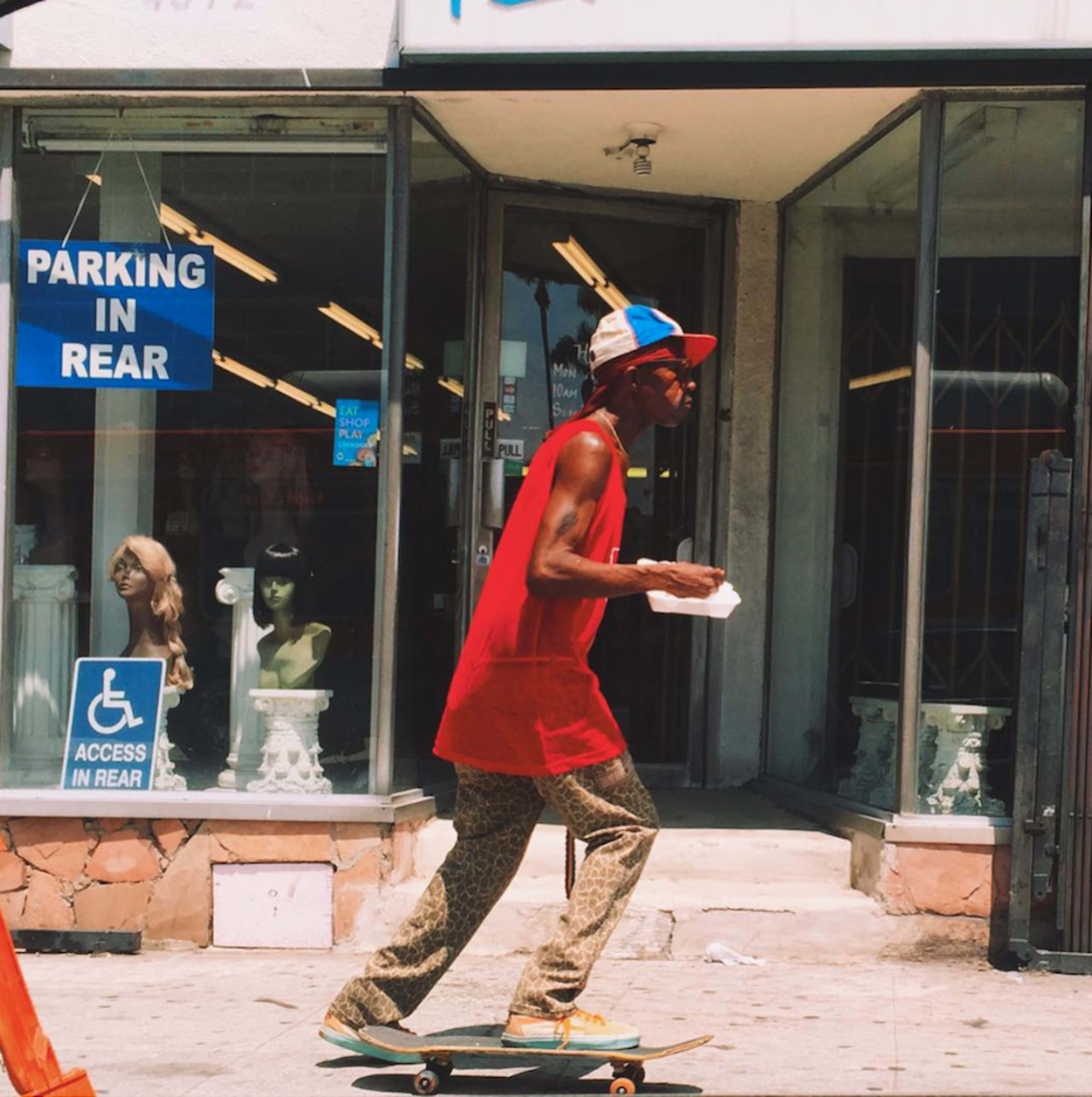 A person skateboards past a store front with a "Parking in Rear" sign and mannequins in the window.