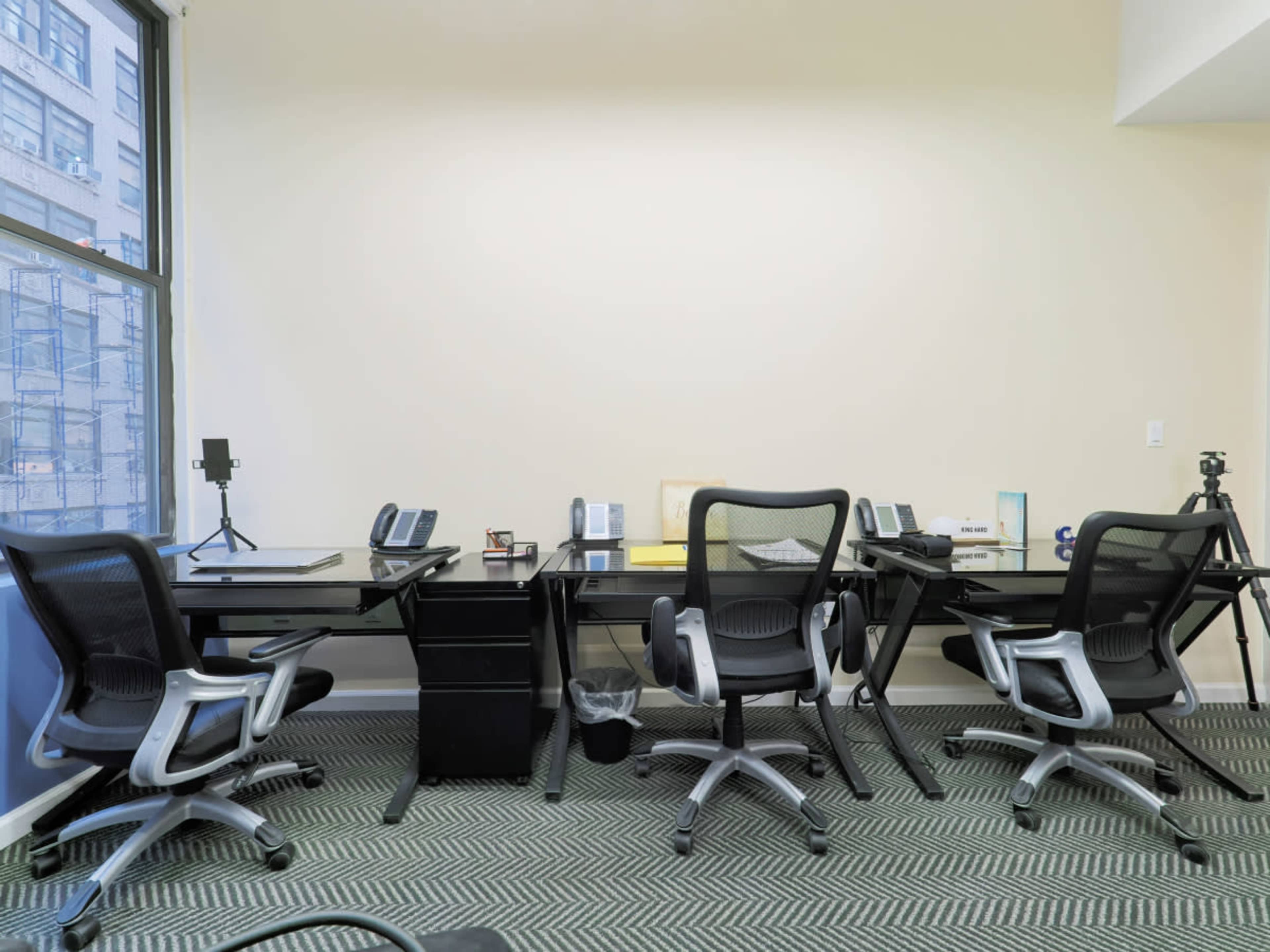 An office space with two desks, each equipped with telephones and other office supplies, surrounded by four office chairs.