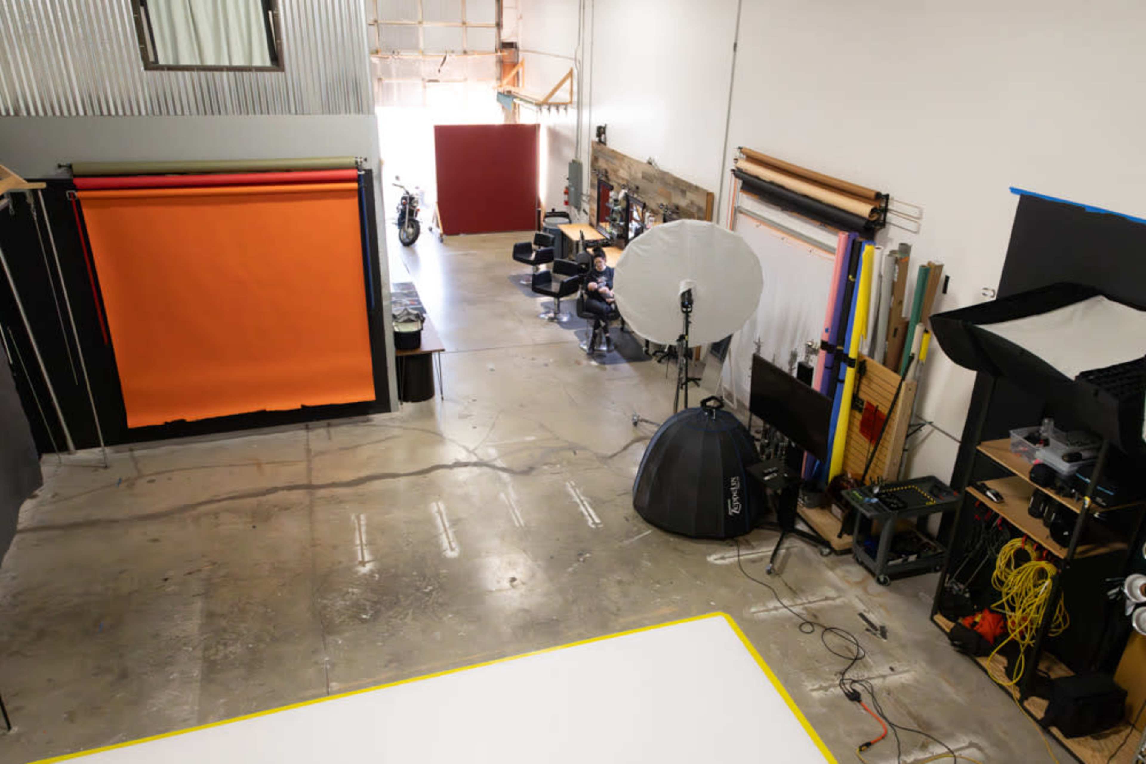 A spacious studio with various colored backdrops, lighting equipment, and seating arrangements, indicating it is set up for photography or video production.