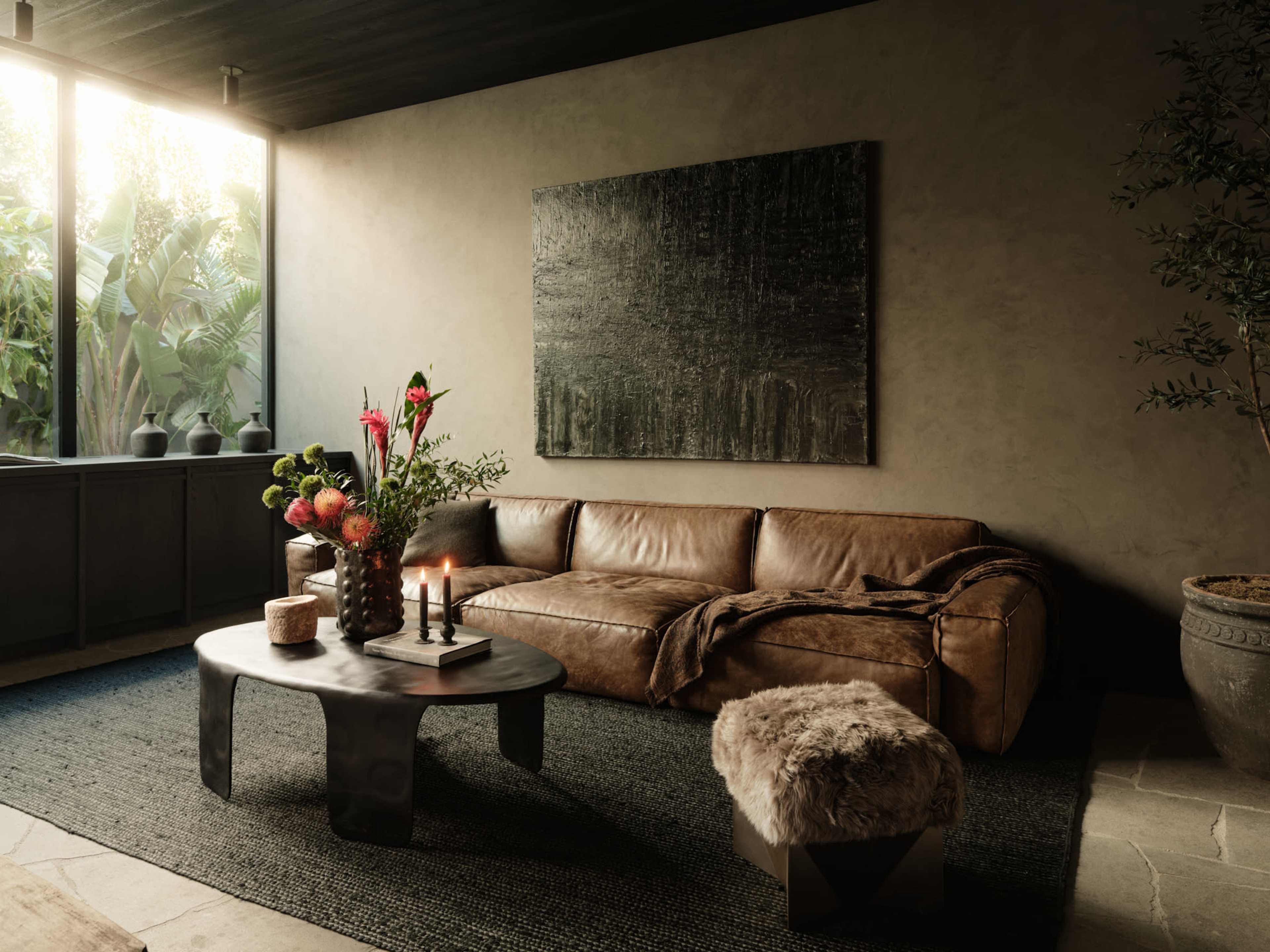 The image depicts a cozy modern living room featuring a leather sofa, a sculptural coffee table, and a floral centerpiece with candles on the table.