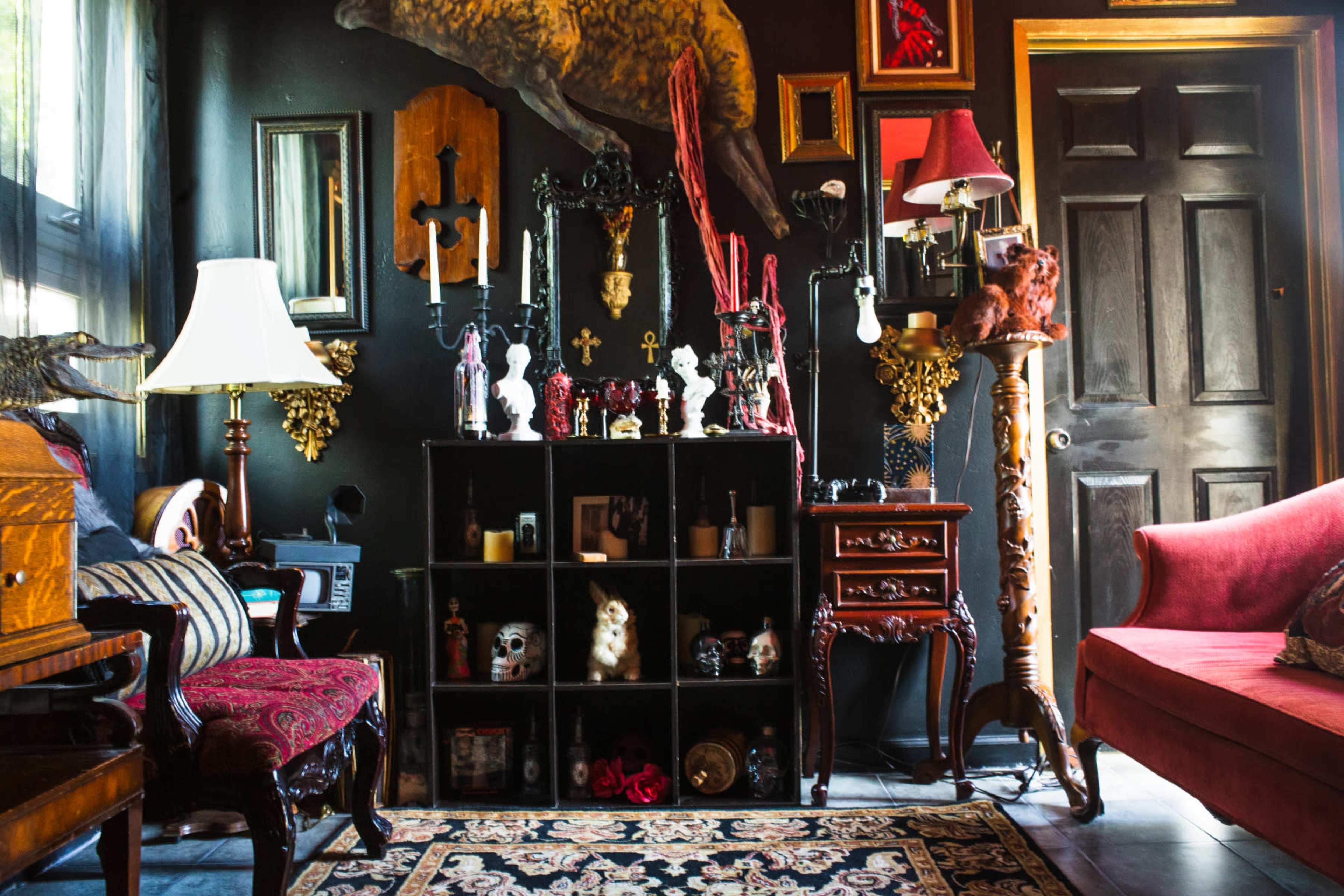 The scene showcases a darkly decorated living room featuring a mix of eclectic furniture, ornate wall decorations, and a bookshelf filled with various decorative items and curios.