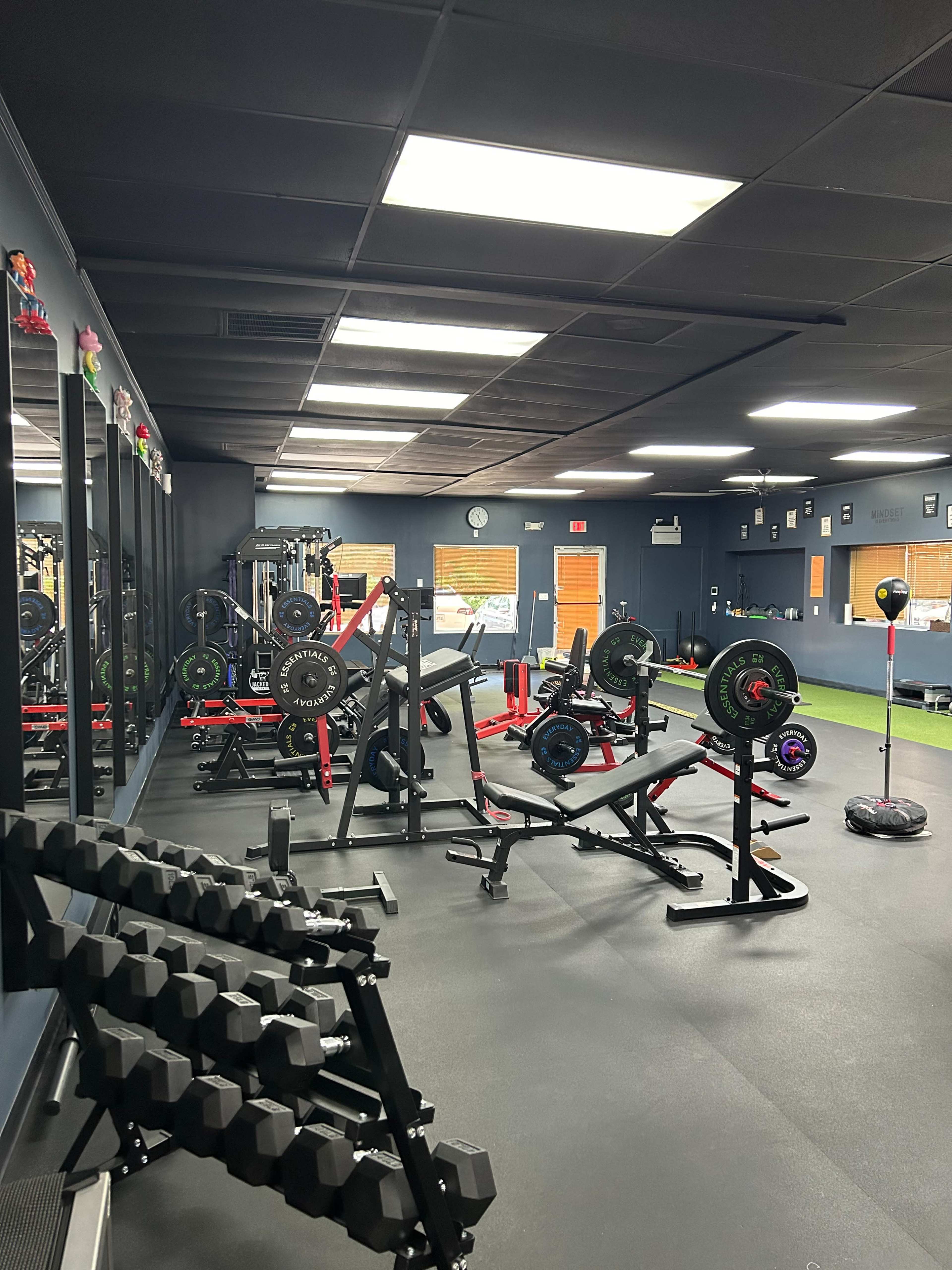 A gym interior with various weightlifting equipment, including benches, barbells, and dumbbells, arranged on a dark floor.