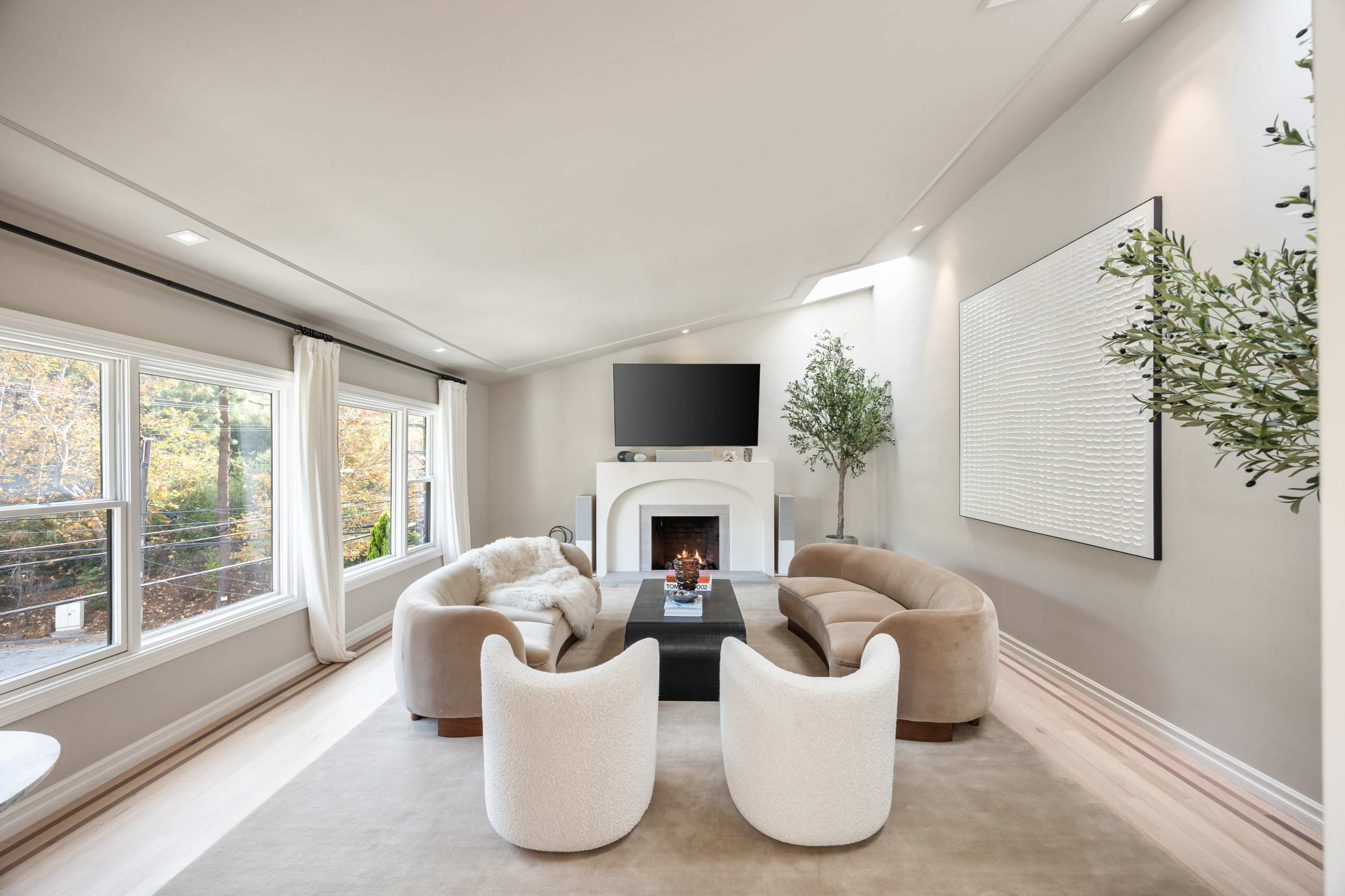 The image depicts a modern living room featuring a fireplace, two curved chairs, a coffee table, and a wall-mounted television.
