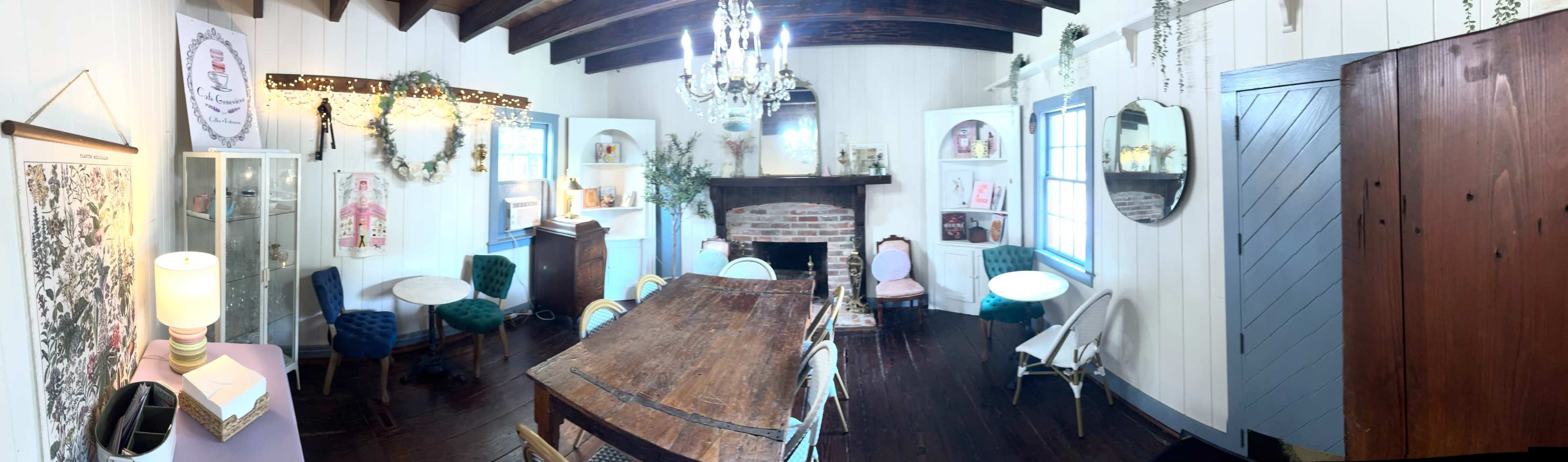 The image depicts a cozy interior room with a long wooden table, a brick fireplace, and a mix of vintage furniture and decor elements.