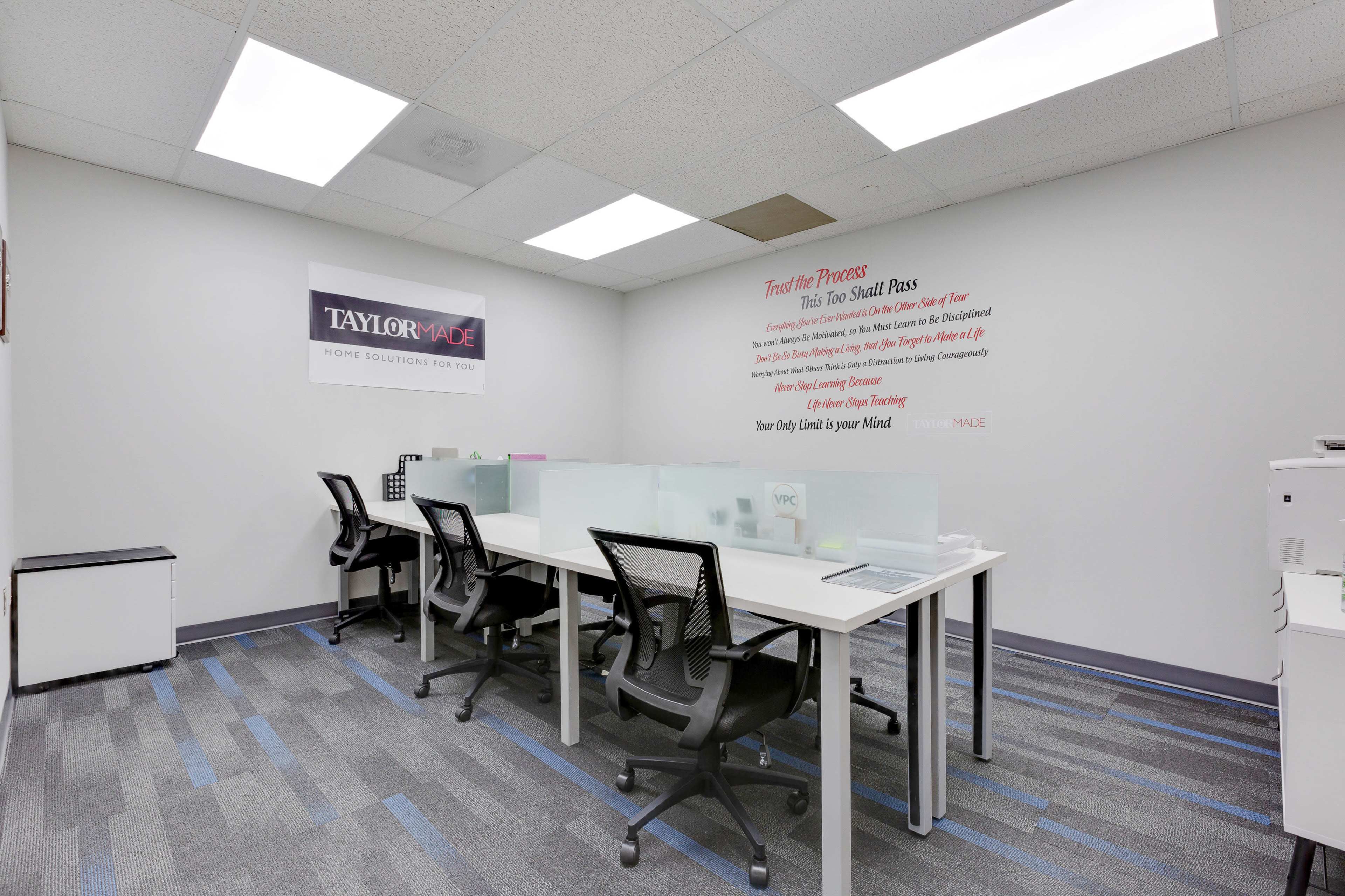 A modern office space with multiple workstations, light-colored walls, and a motivational sign on the wall.