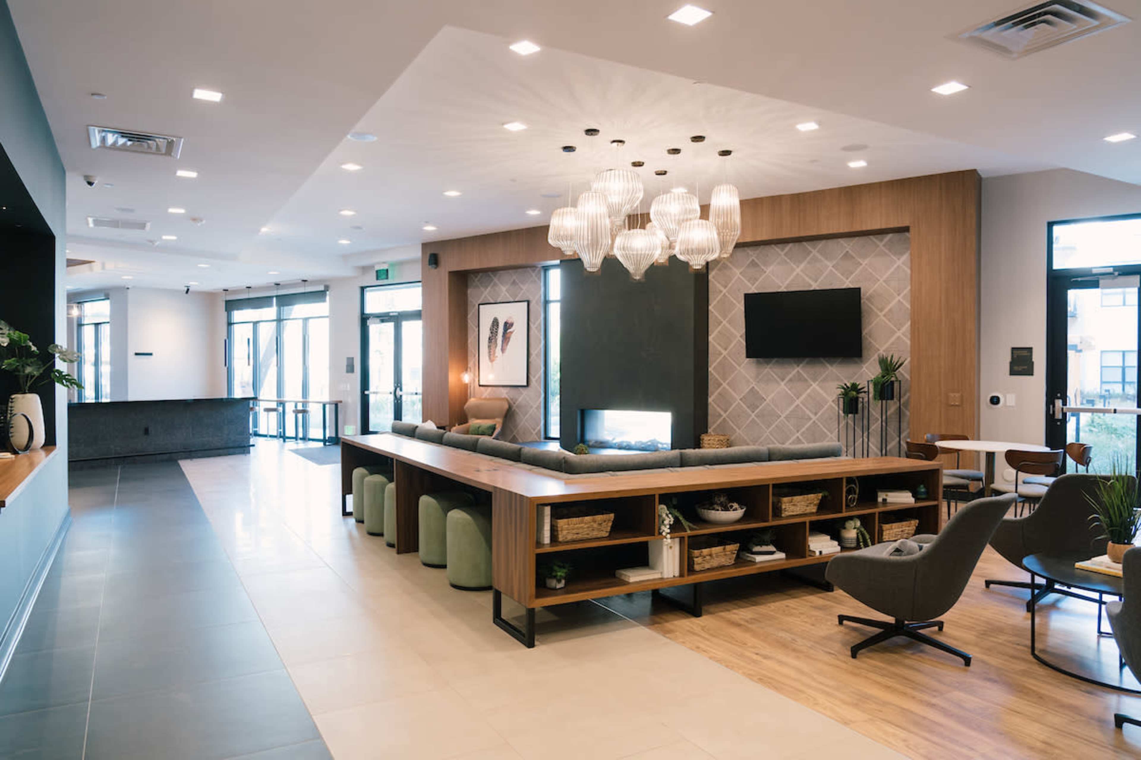 A modern lobby area featuring a long table with seating, a decorative fireplace, and a geometric accent wall.