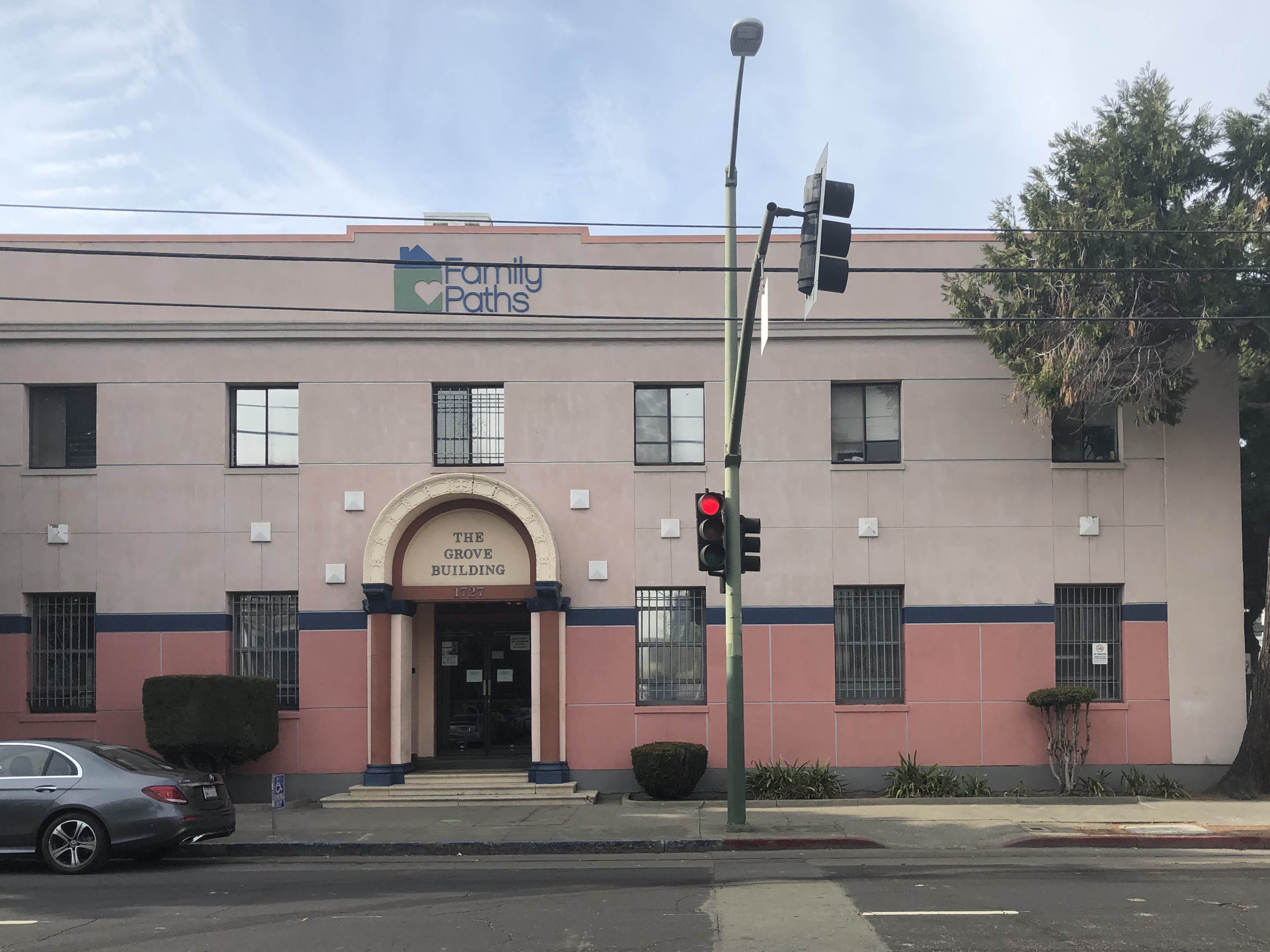 A two-story building with a sign reading "Family Paths" and "THE GROVE BUILDING," featuring a pink exterior and a green traffic light in front.