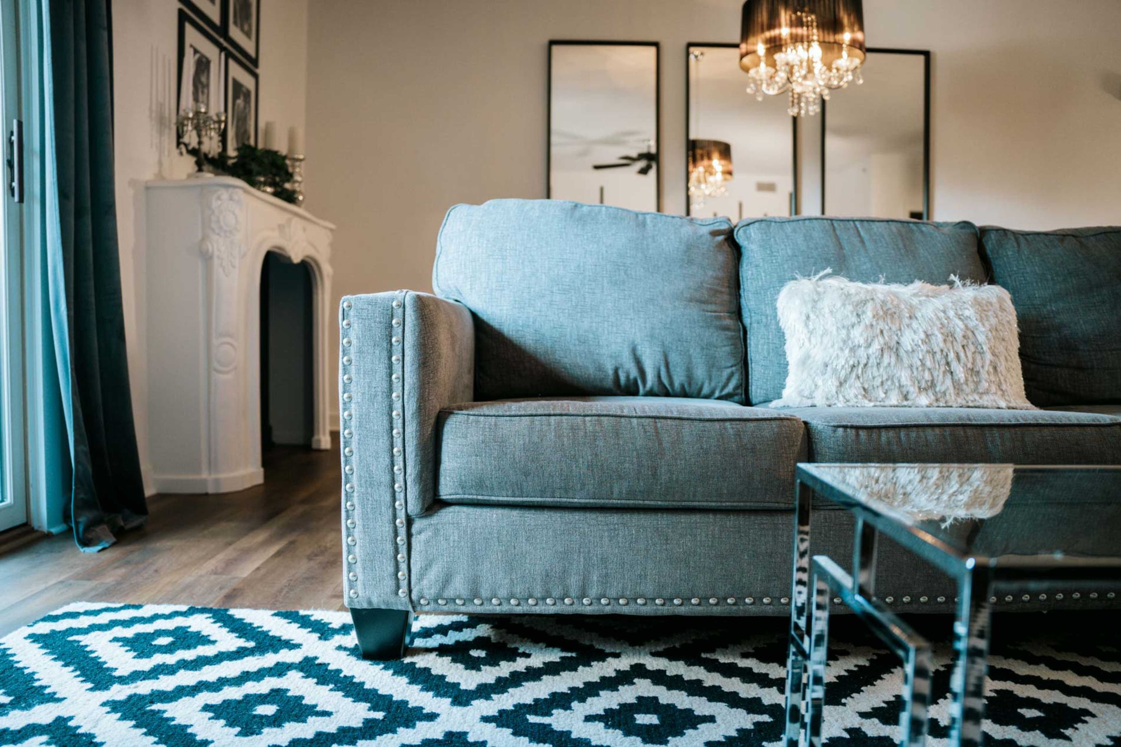 A gray sofa with a decorative pillow sits on a black and white patterned rug in a modern living room featuring a mirrored wall and a chandelier.