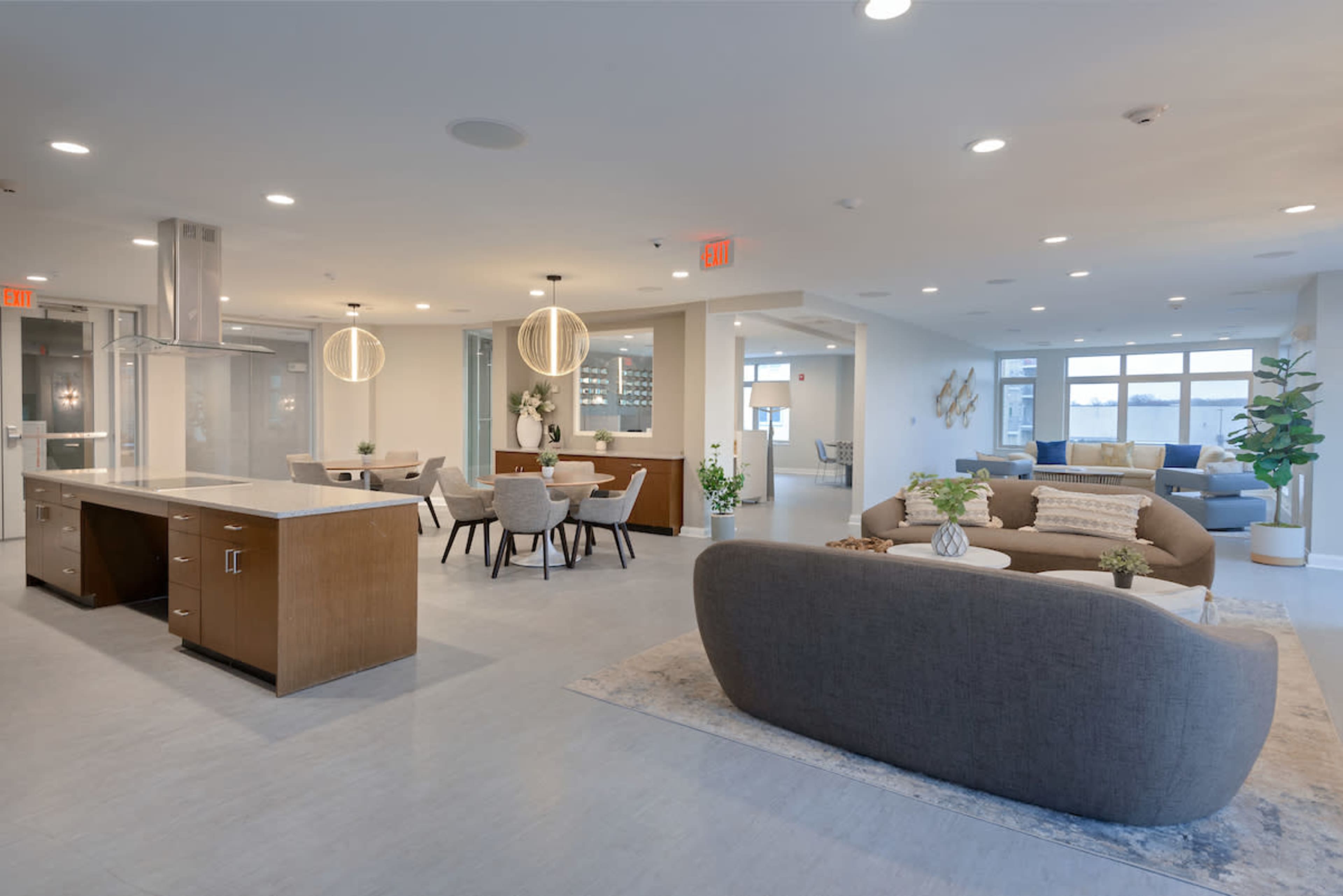 A modern open-concept living space features a kitchen island, dining area, and comfortable seating arrangement with large windows allowing natural light.
