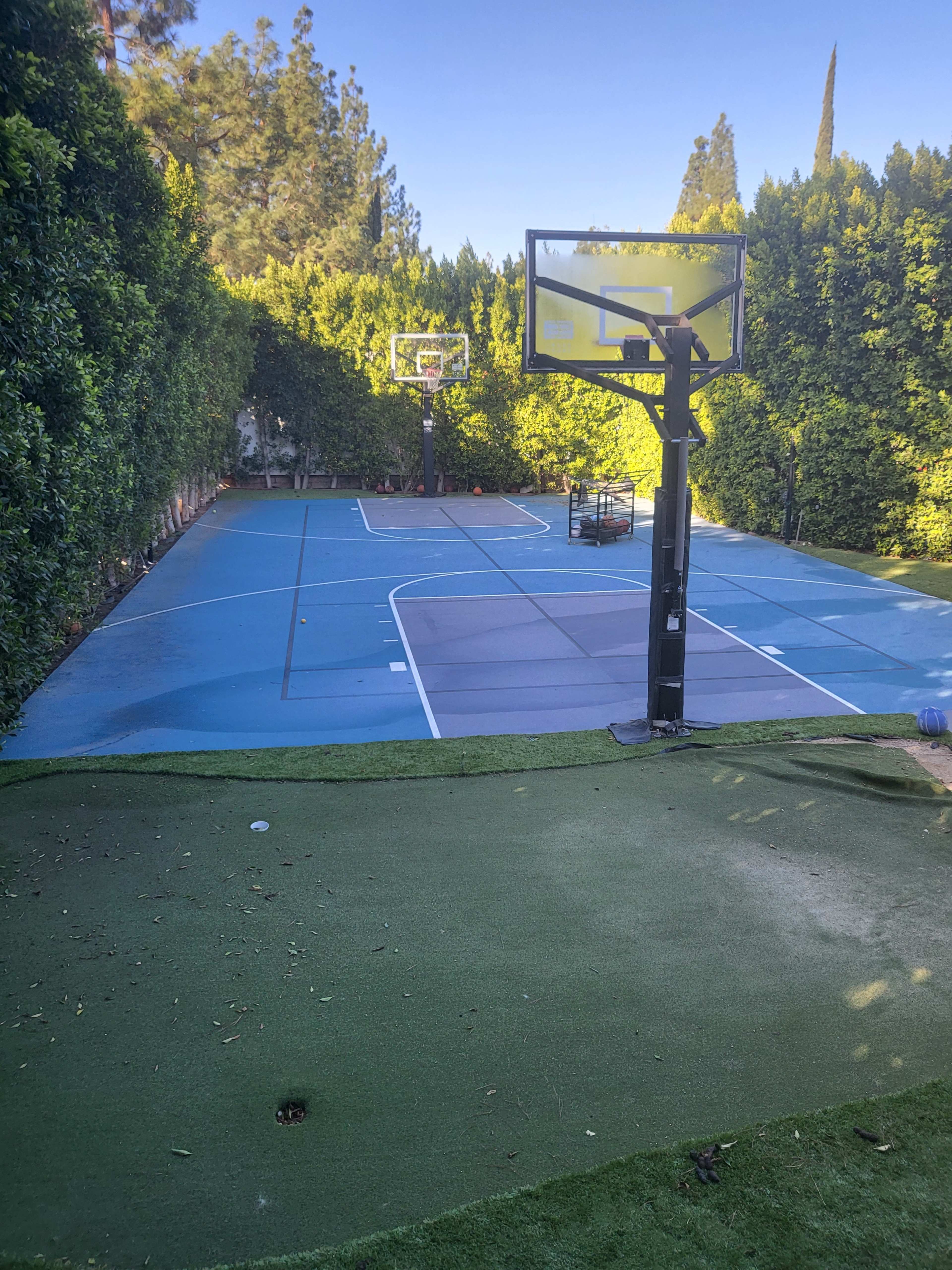 A private outdoor basketball court surrounded by tall green hedges.
