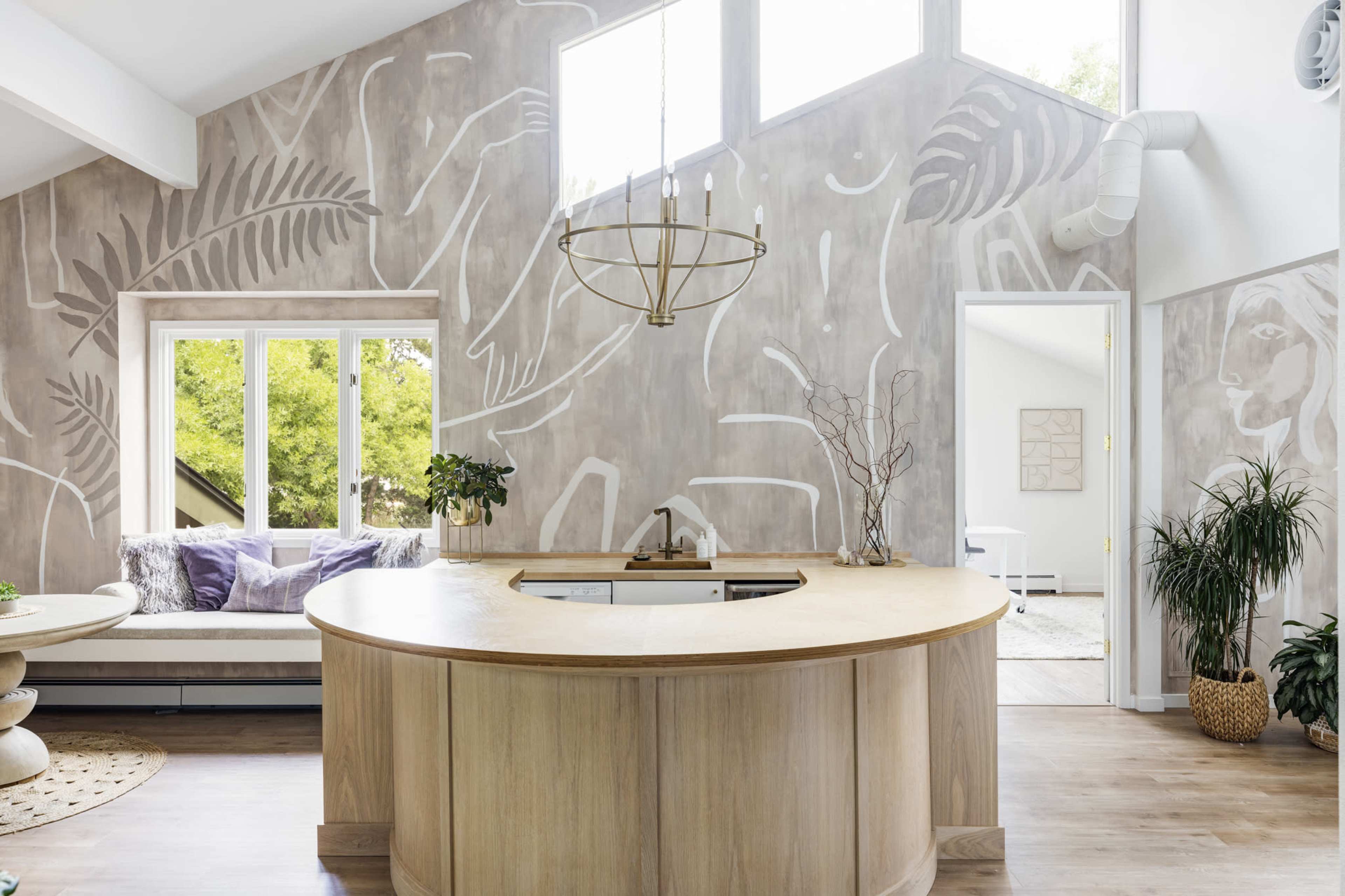 The image features a modern kitchen with a curved wooden countertop, surrounded by a wall adorned with abstract white line art and a large window providing natural light.