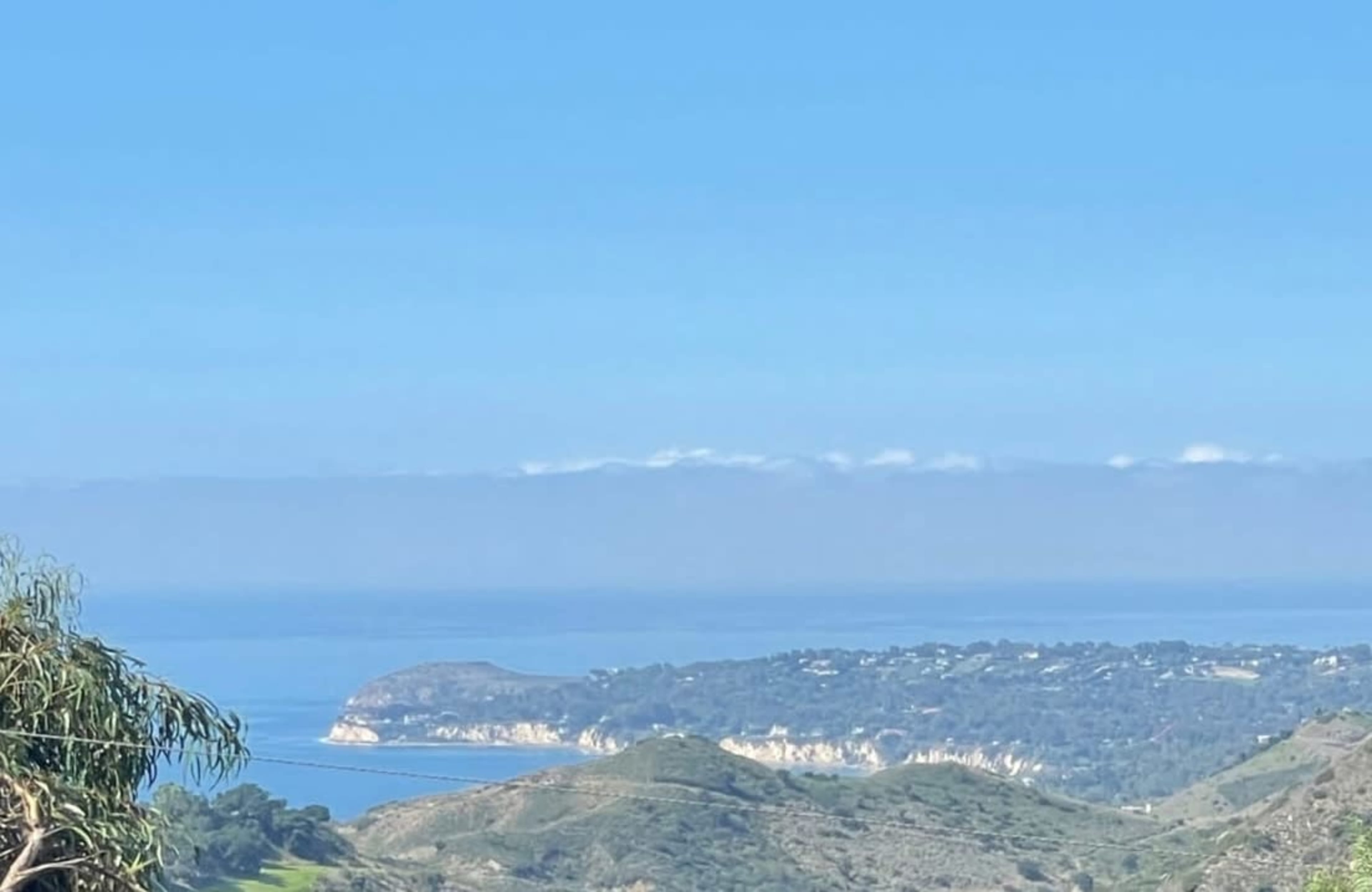 A coastal landscape with rolling hills and a view of the ocean under a clear blue sky.