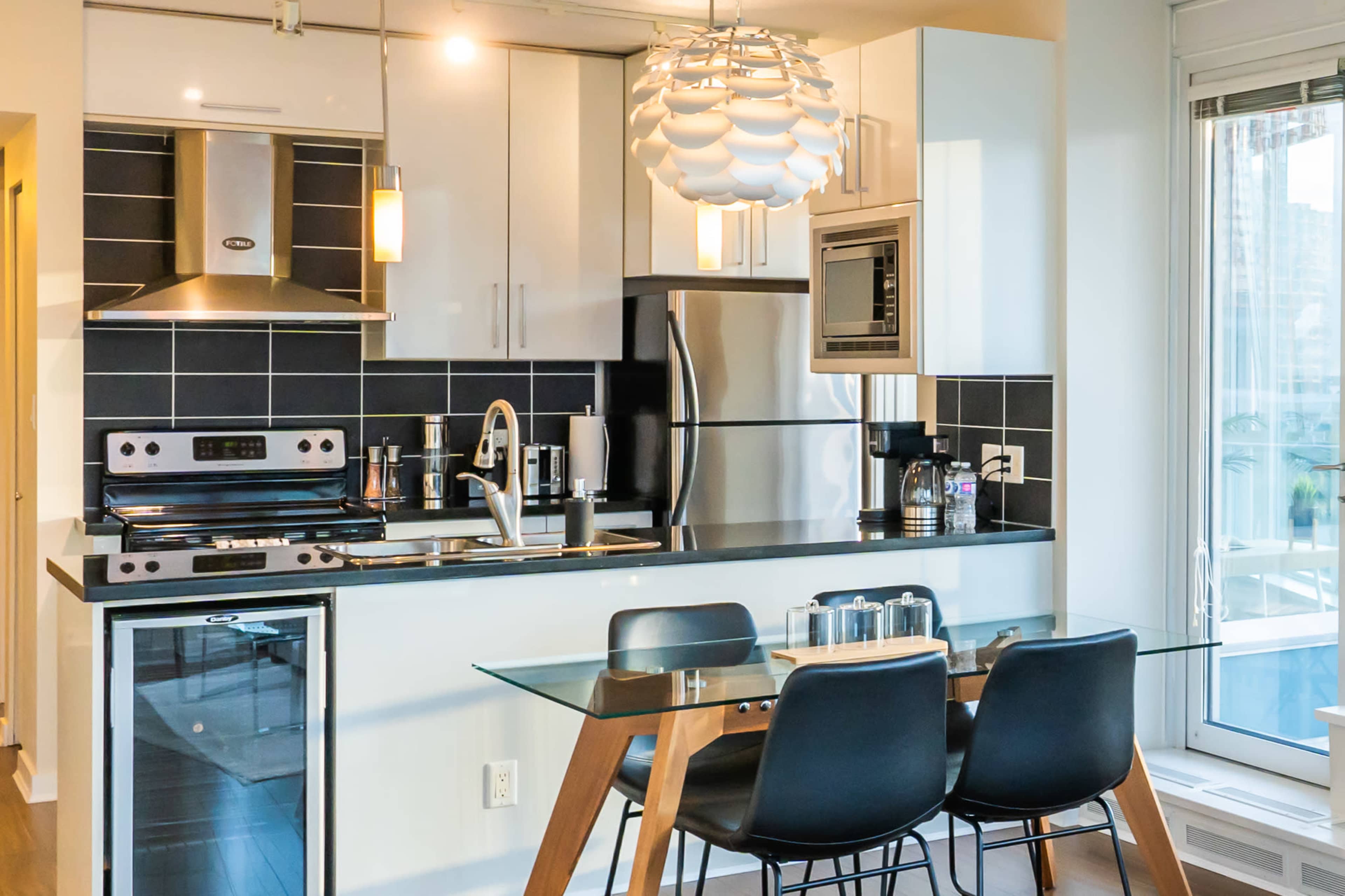 A modern kitchen features stainless steel appliances, black and white cabinetry, and a glass dining table with black chairs.