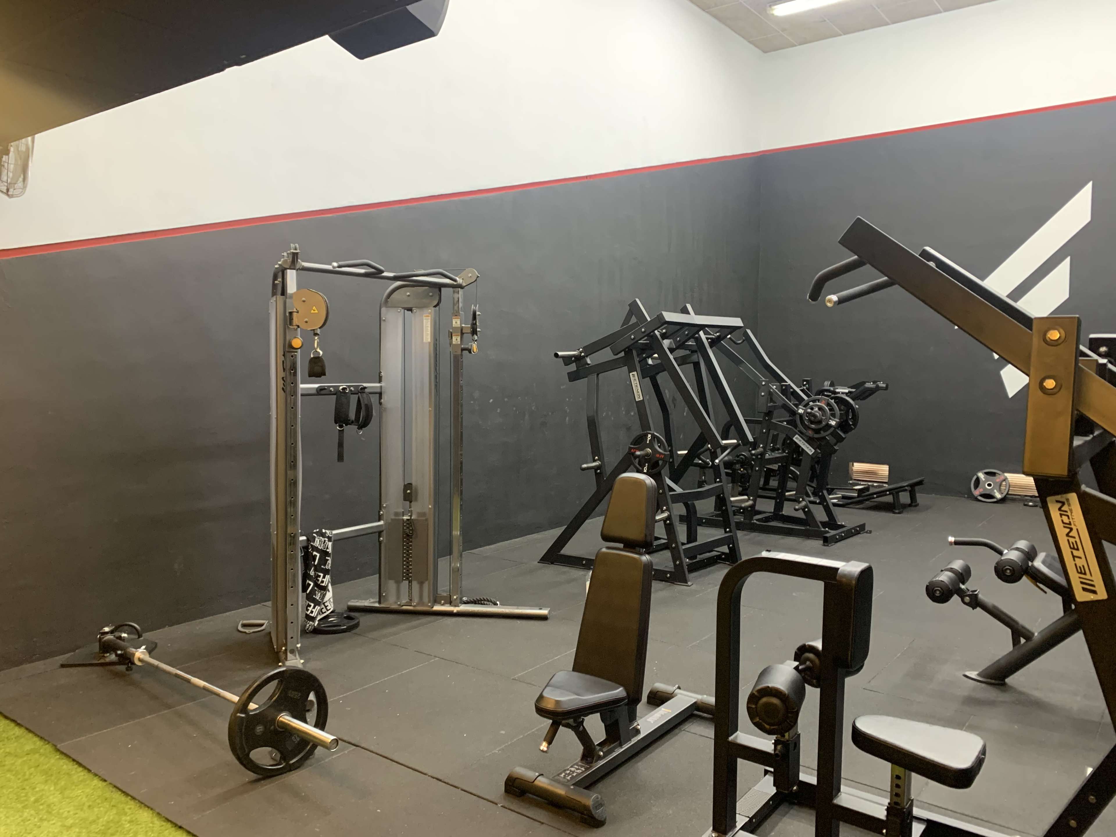 A gym interior with various exercise equipment, including a cable machine, weight bench, and free weights.