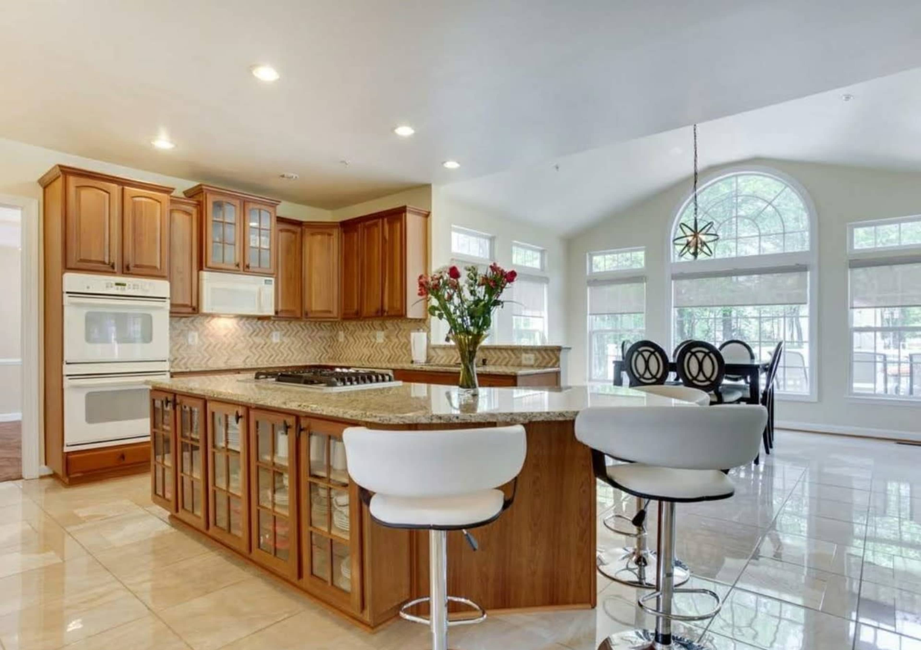 A modern kitchen with wooden cabinetry, a central island with bar stools, and large windows letting in natural light.
