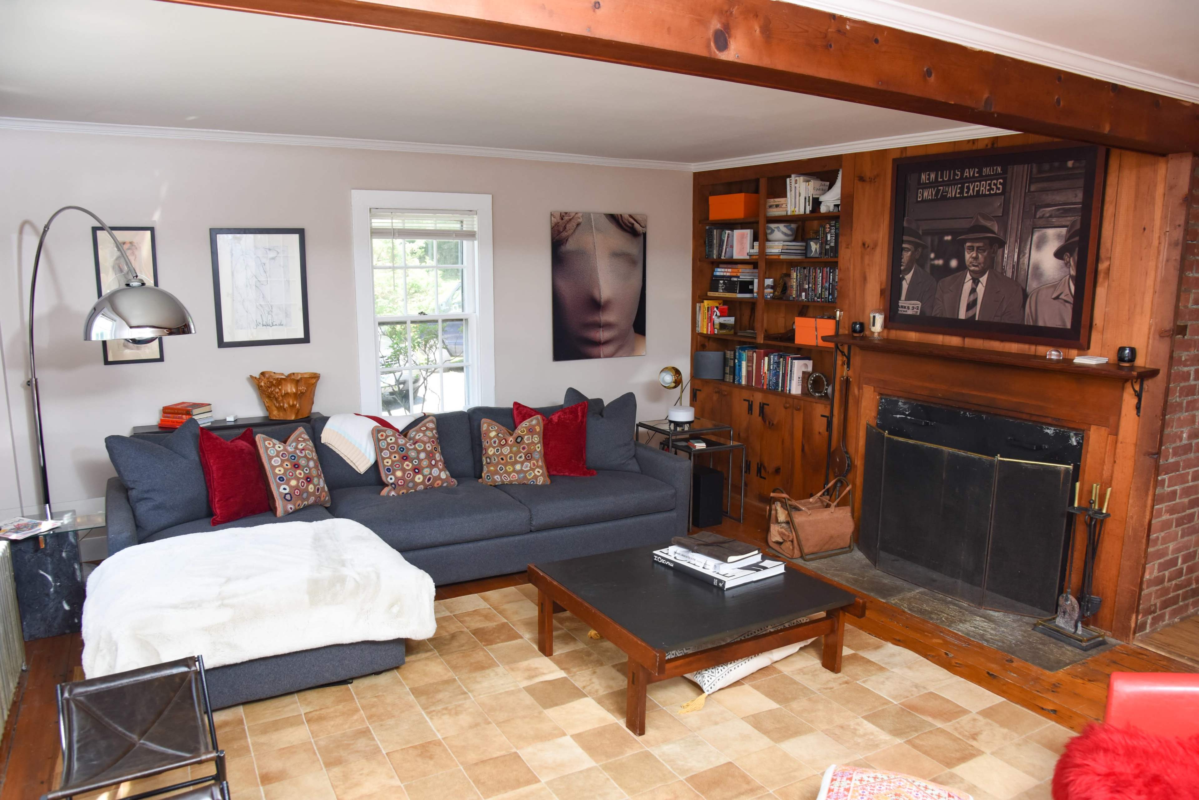 The living room features a dark gray sectional sofa adorned with colorful pillows, a wooden coffee table, and a fireplace integrated into a brick wall.