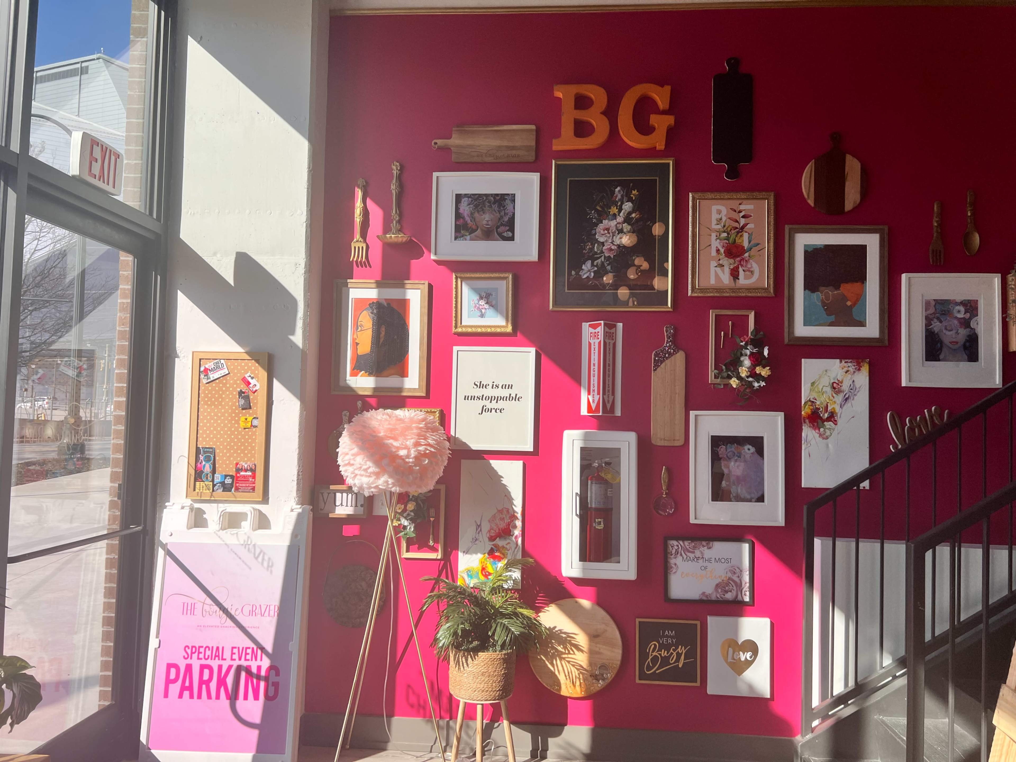 The image features a vibrant pink wall adorned with various framed artworks, decorative items, and a bulletin board, creating an eclectic gallery display.