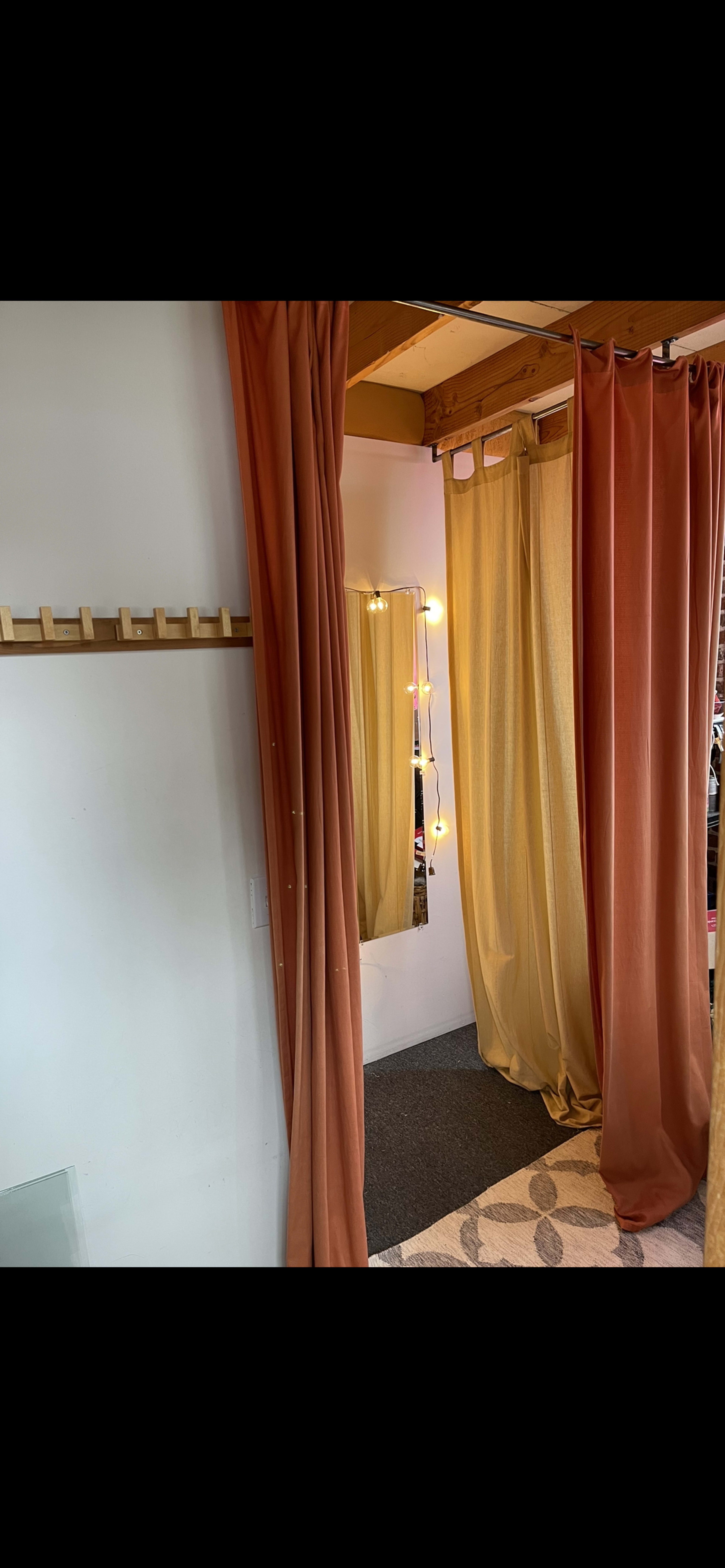 A small room divided by flowing orange and yellow curtains, with a mirror and string lights visible on the wall.