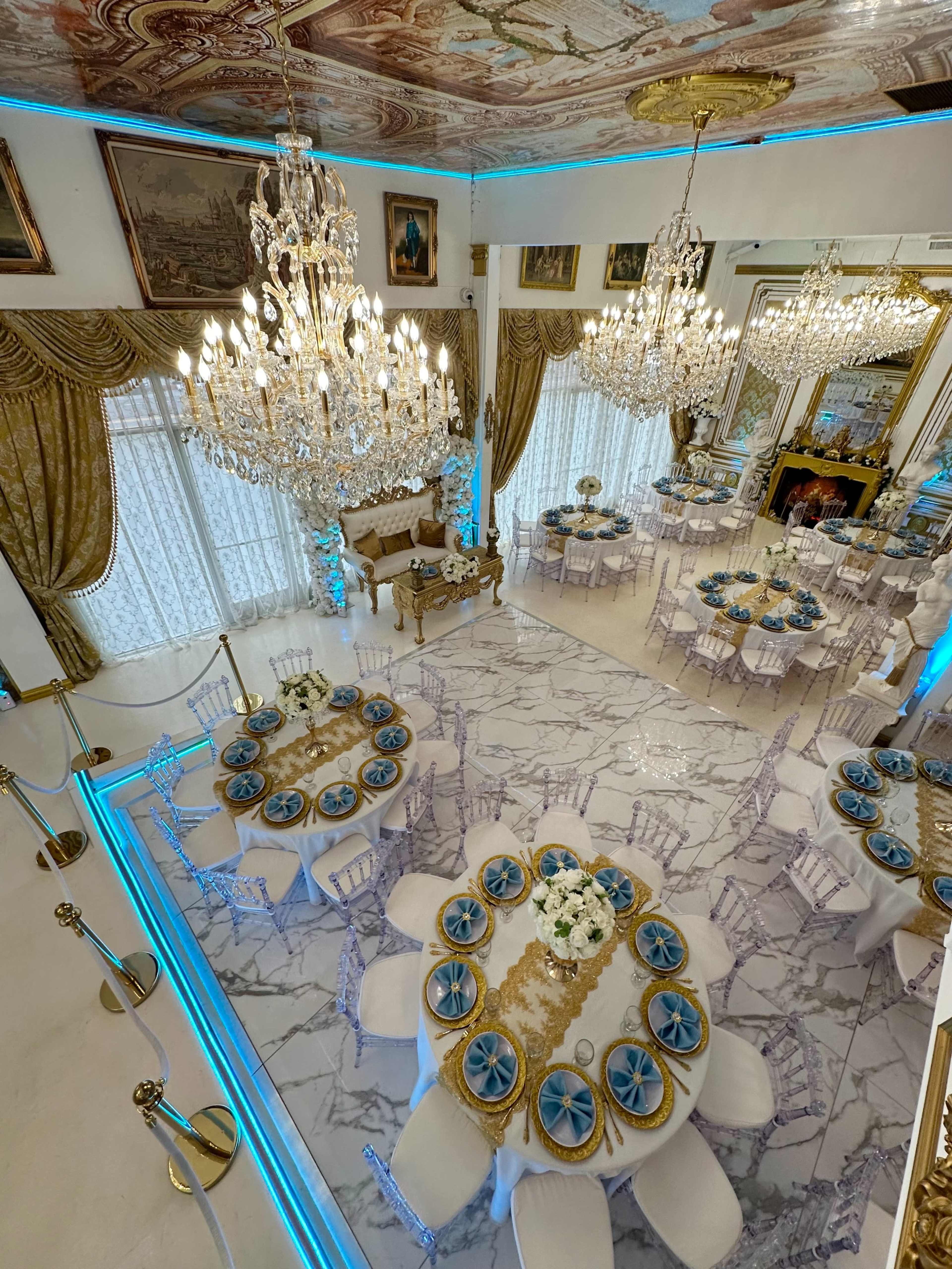 The image shows an elegant dining hall adorned with chandeliers, ornate table settings, and blue-lit decor on marble flooring.