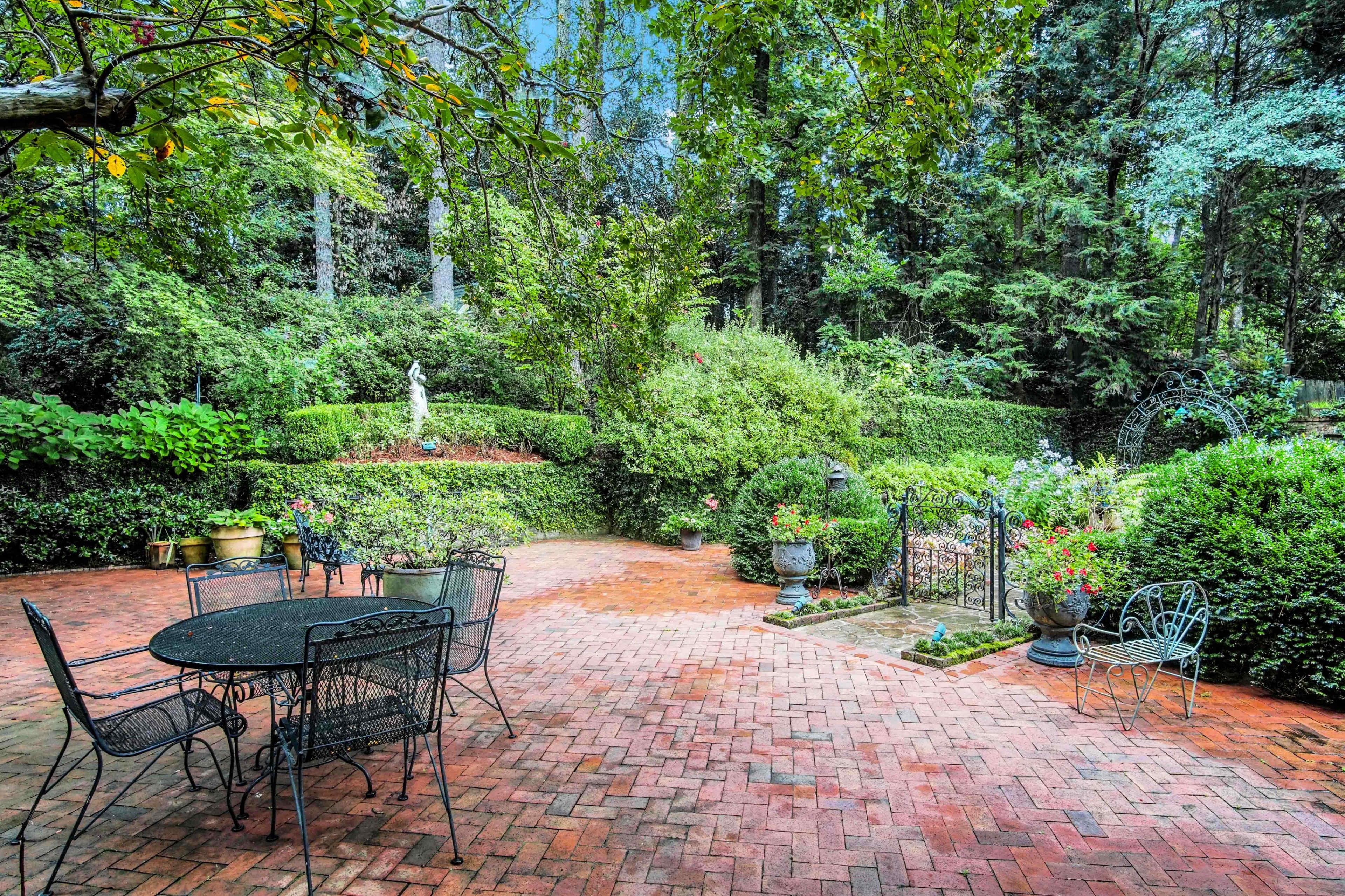 A brick patio surrounded by lush greenery and garden features, including a statue and potted plants.