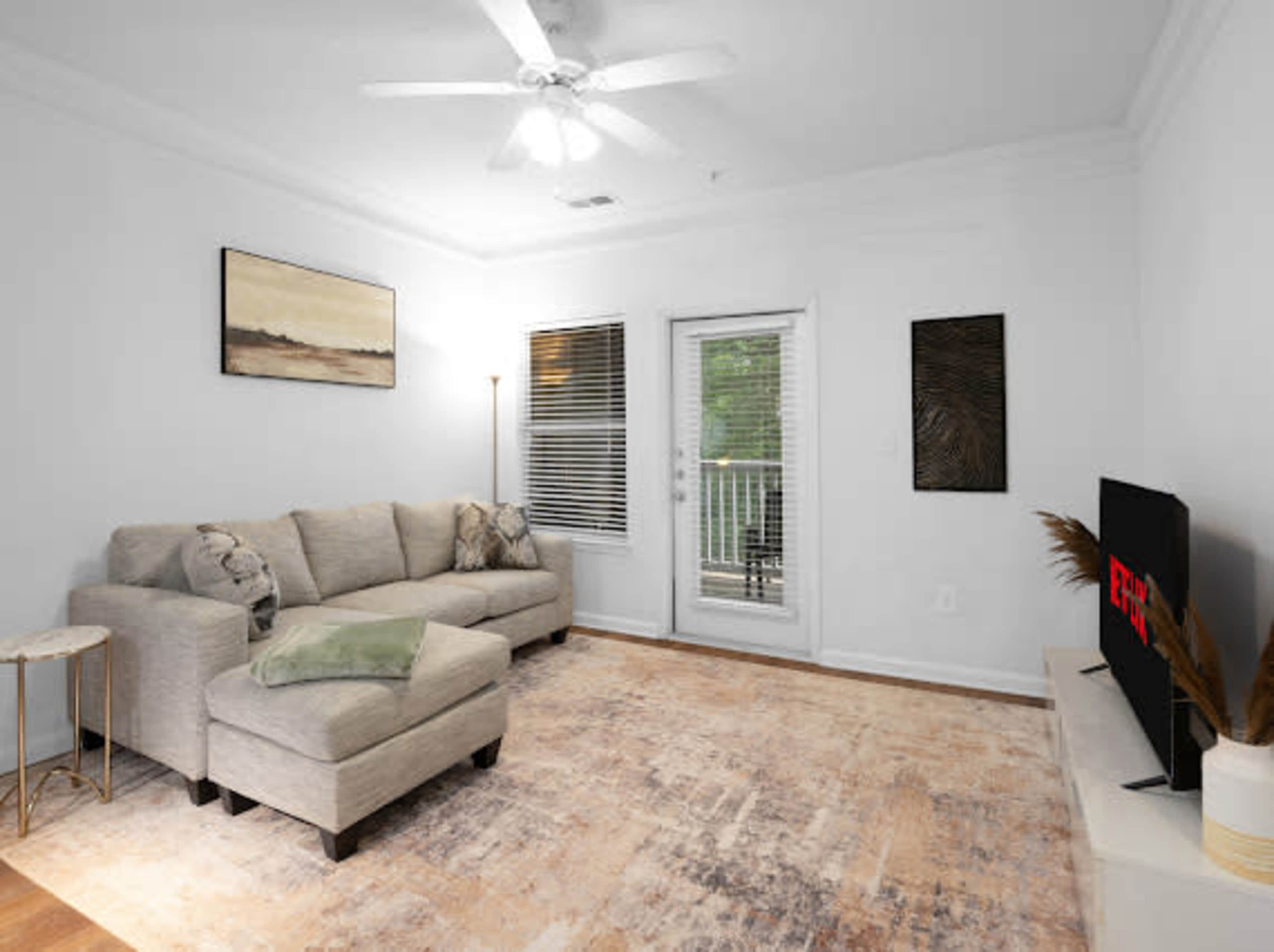 The living room features a light-colored sectional sofa, a coffee table, a wall-mounted television, and a set of sliding glass doors leading to a balcony.