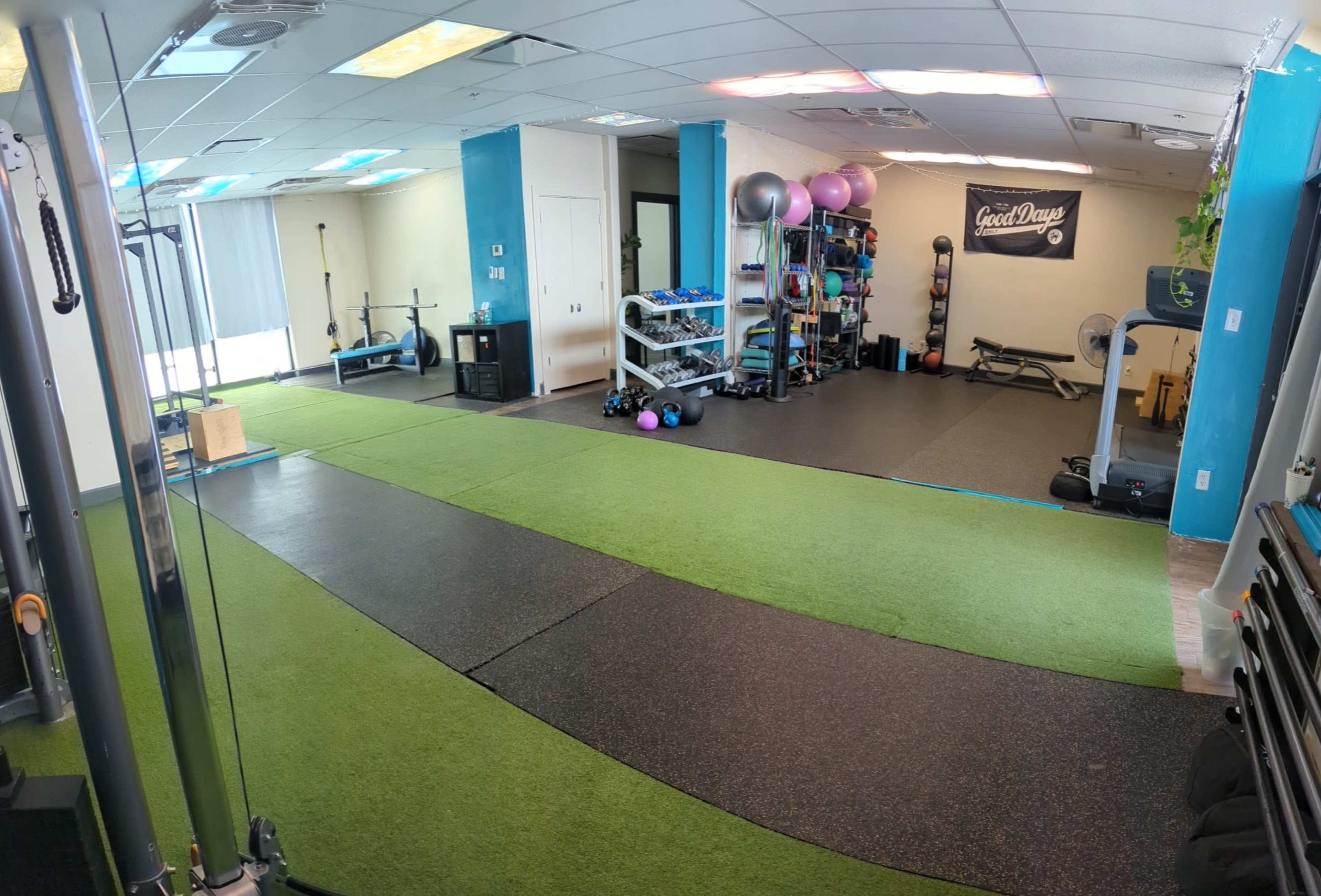 A gym interior featuring green turf flooring, various exercise equipment, and workout stations arranged in a spacious layout.