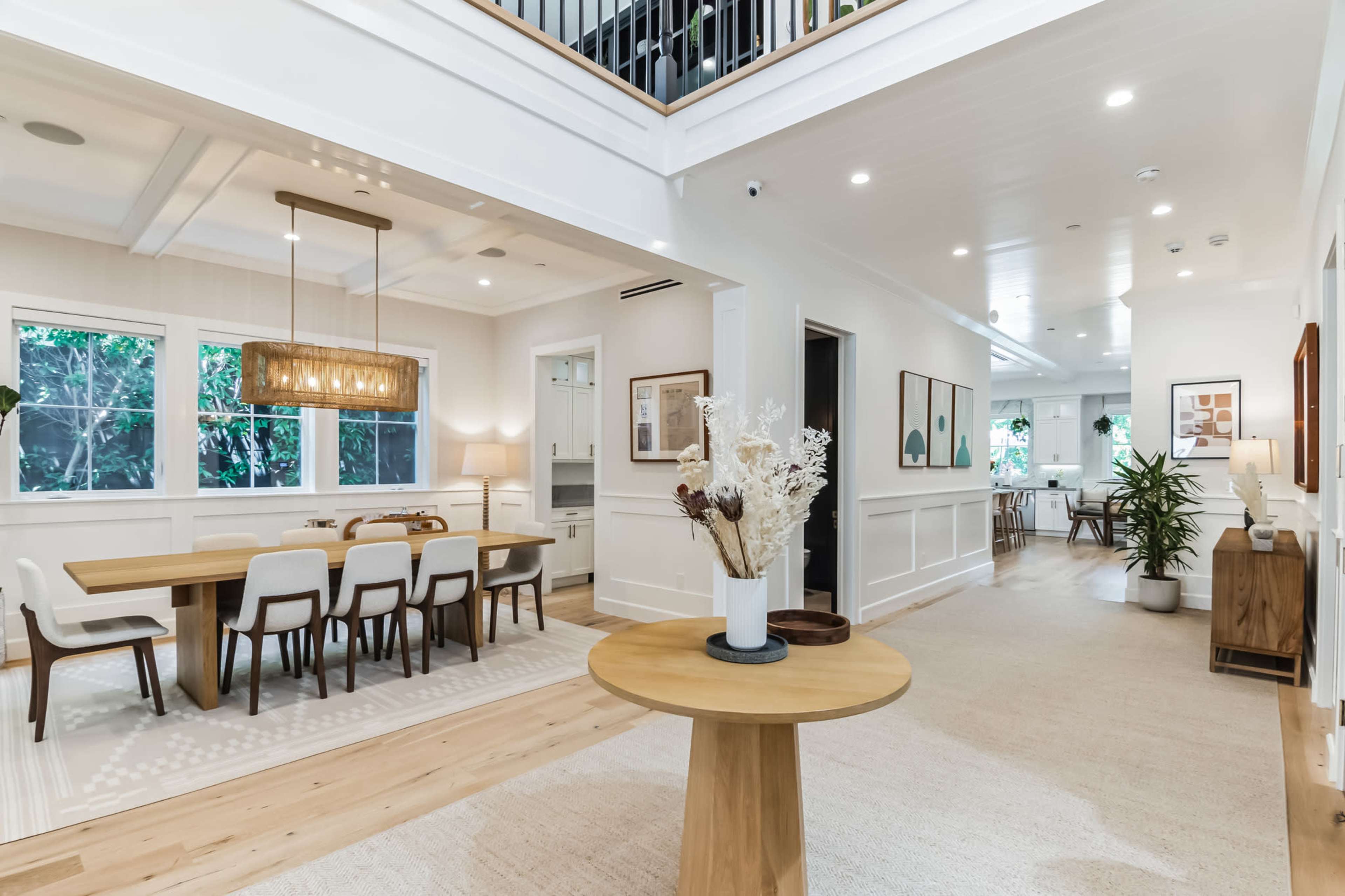 A spacious, well-lit entryway featuring a circular wooden table, a dining area with a large table and chairs, and a view of additional rooms in a modern home.