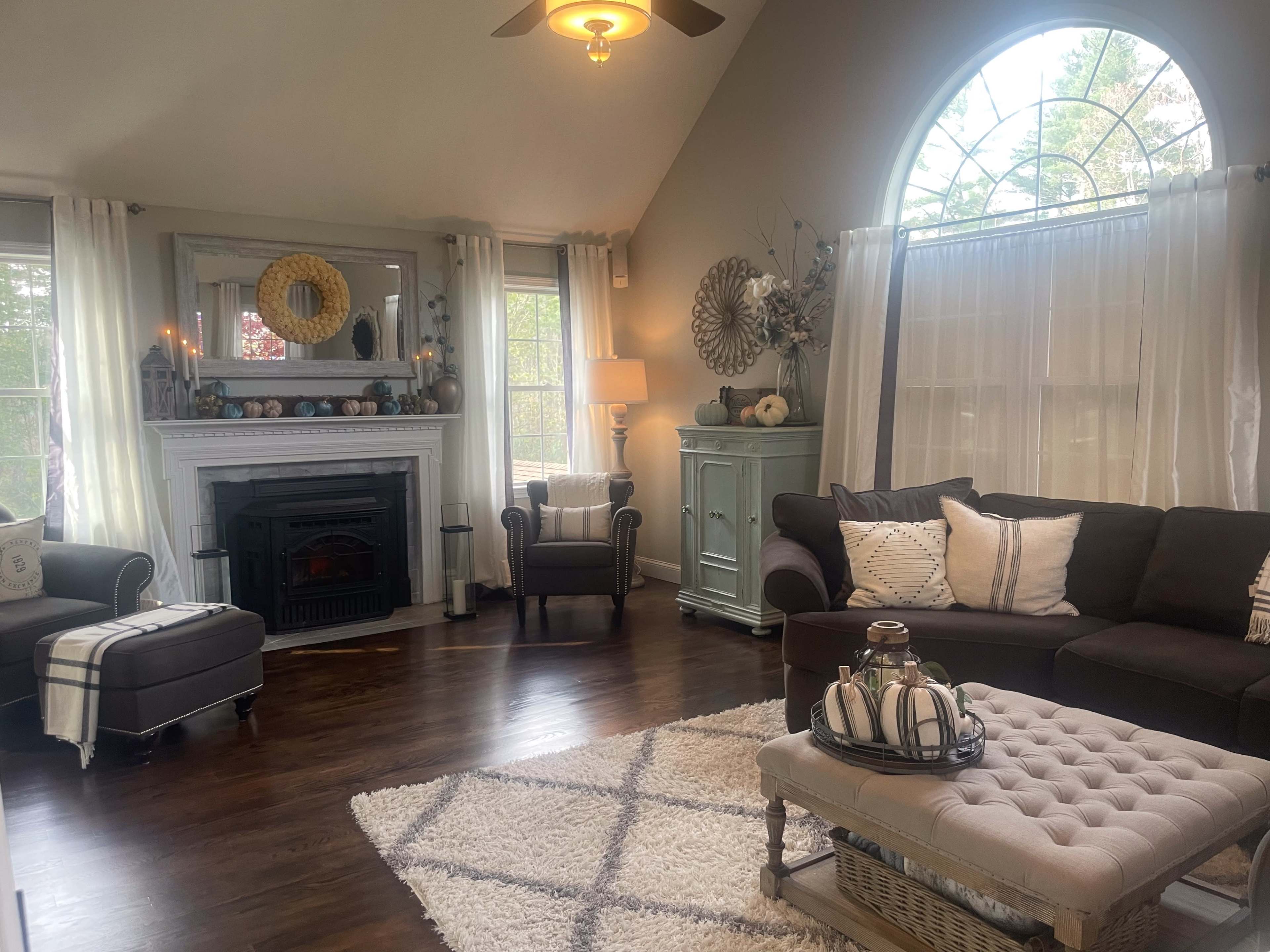 The living room features a dark sectional sofa, a light-colored coffee table with decorative items, and large windows allowing natural light to illuminate the space.