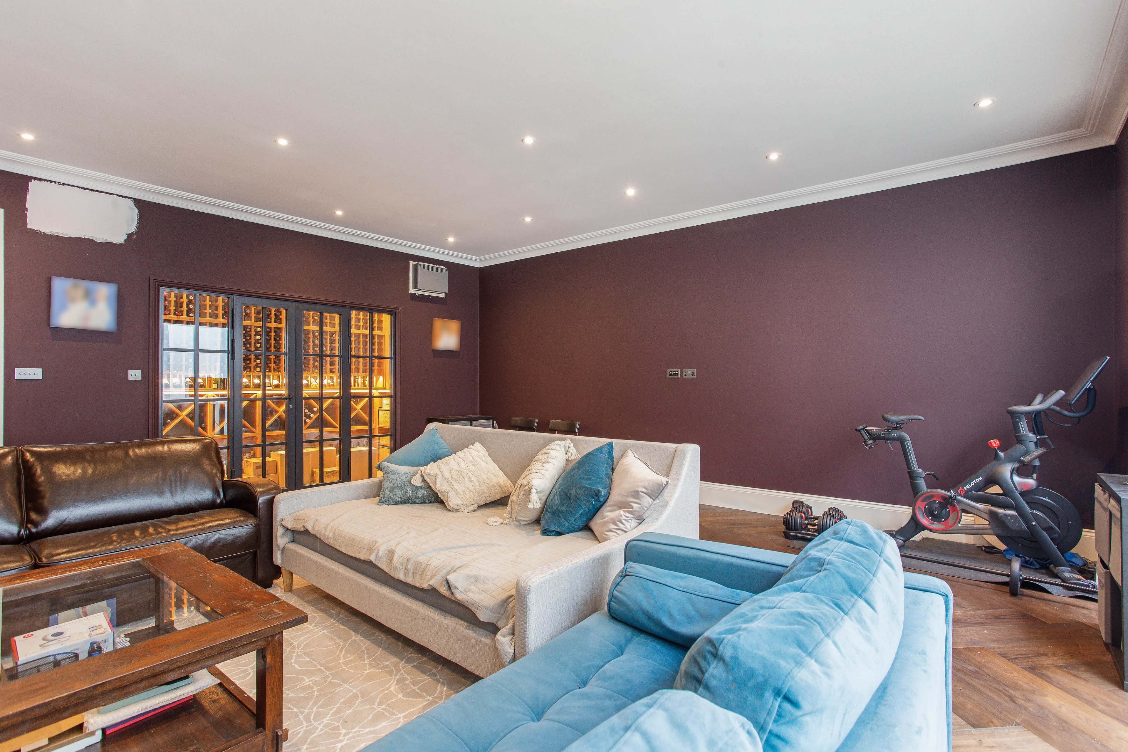 A living room featuring a blue couch, a beige sofa with decorative cushions, a wooden coffee table, and a view of a dining area through glass doors.