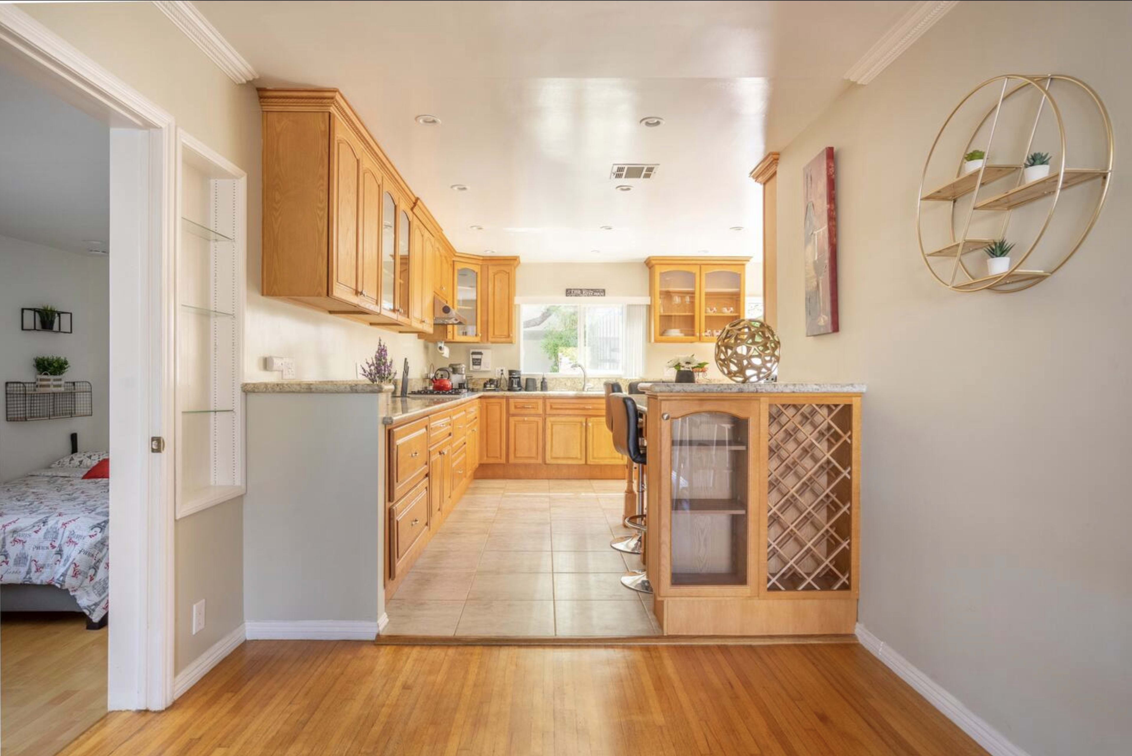A kitchen area features wooden cabinets, a tiled floor, and a bar with stools adjacent to a dining space.