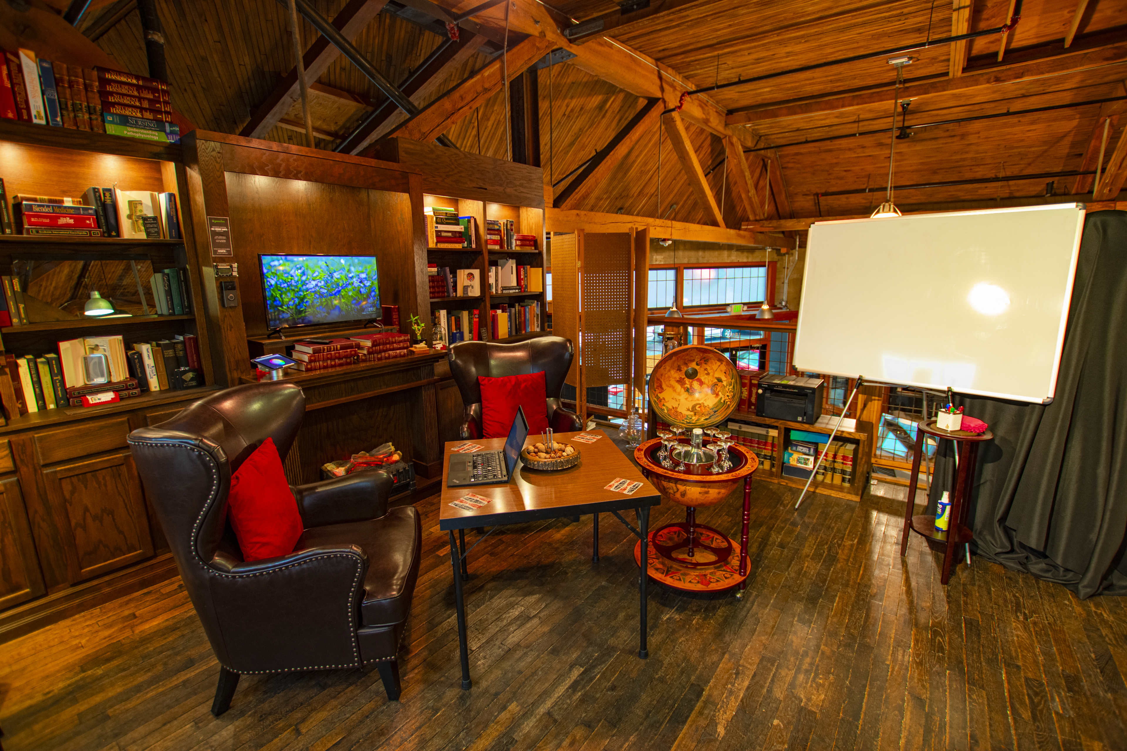 A cozy, wooden-paneled room with two armchairs, a table, a globe, a whiteboard, and bookshelves filled with books.