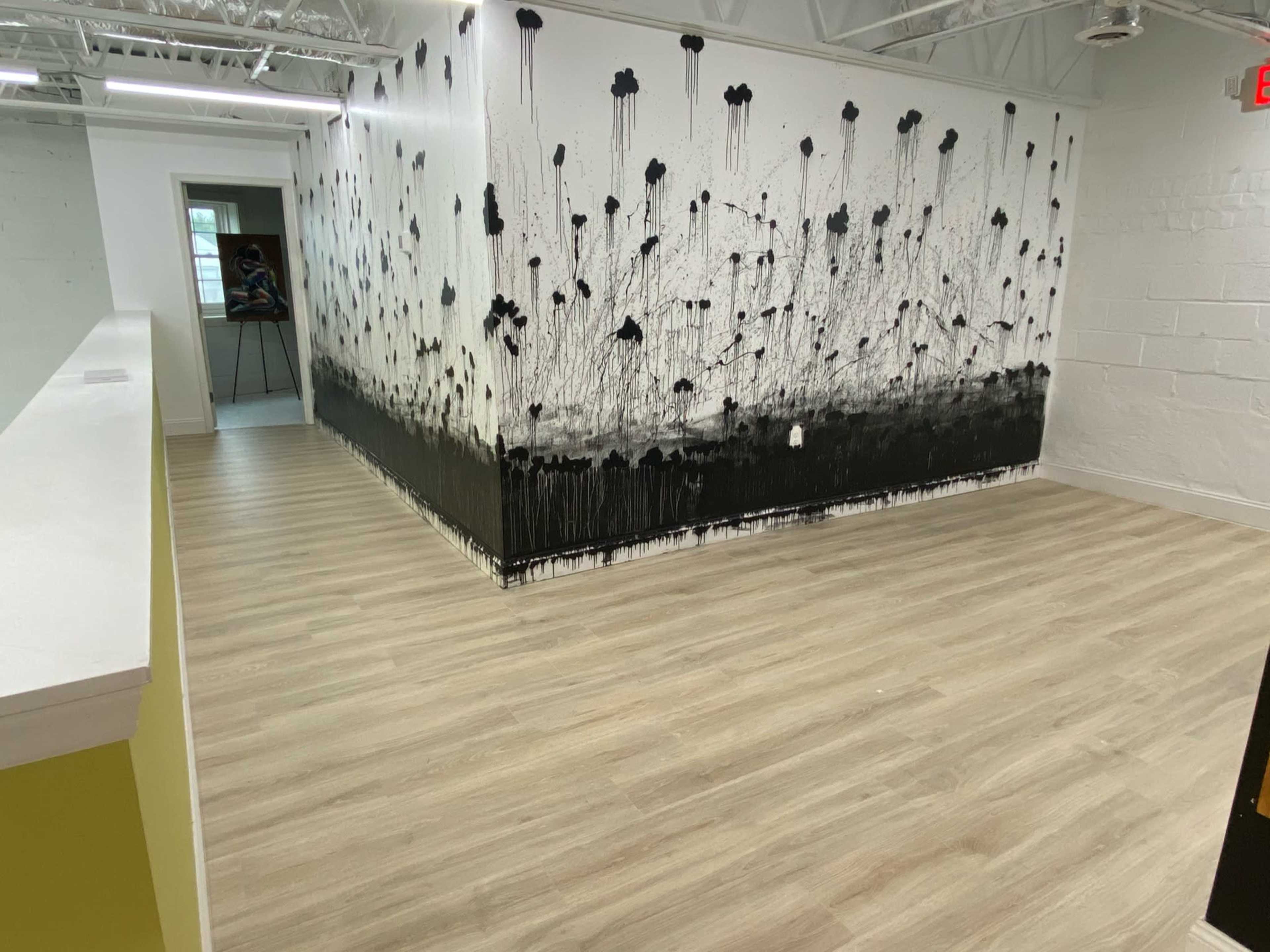 A spacious room with a wall featuring black paint drips resembling flowers, and light-colored wooden flooring.