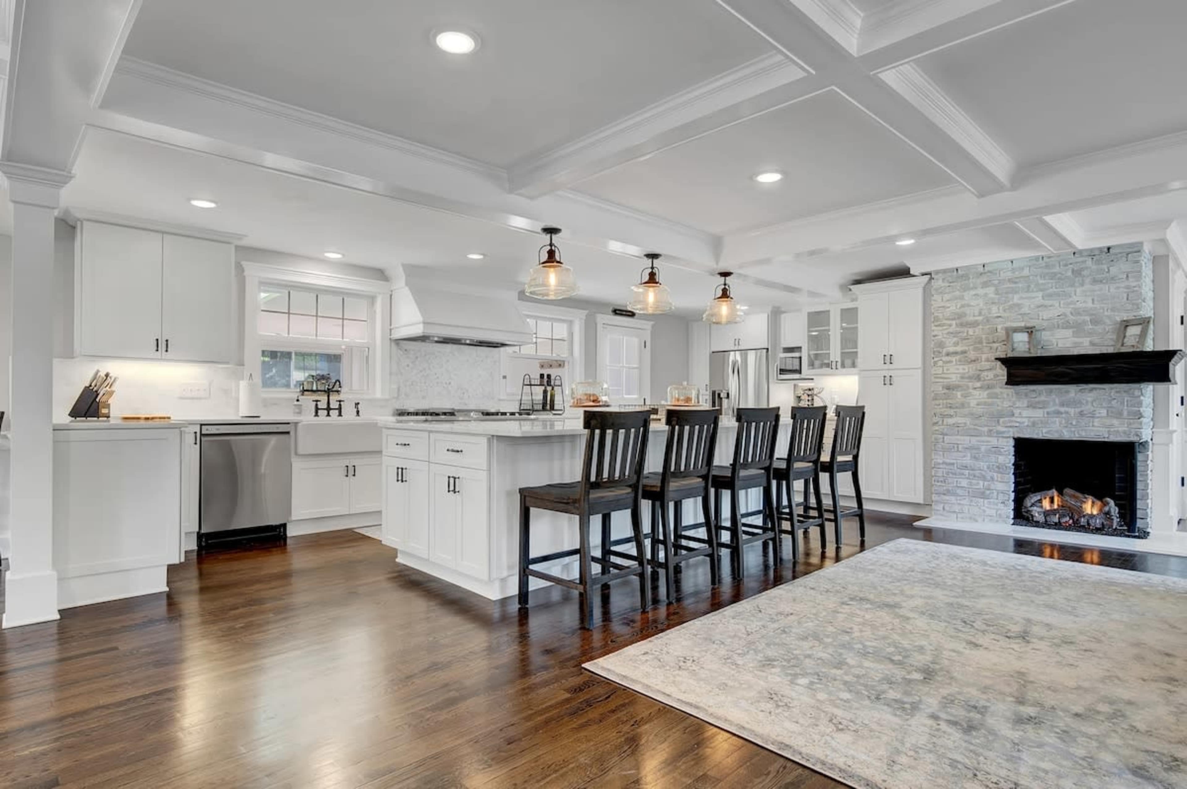 A modern kitchen features white cabinetry, a large central island with bar seating, and a cozy stone fireplace with a warm glow.
