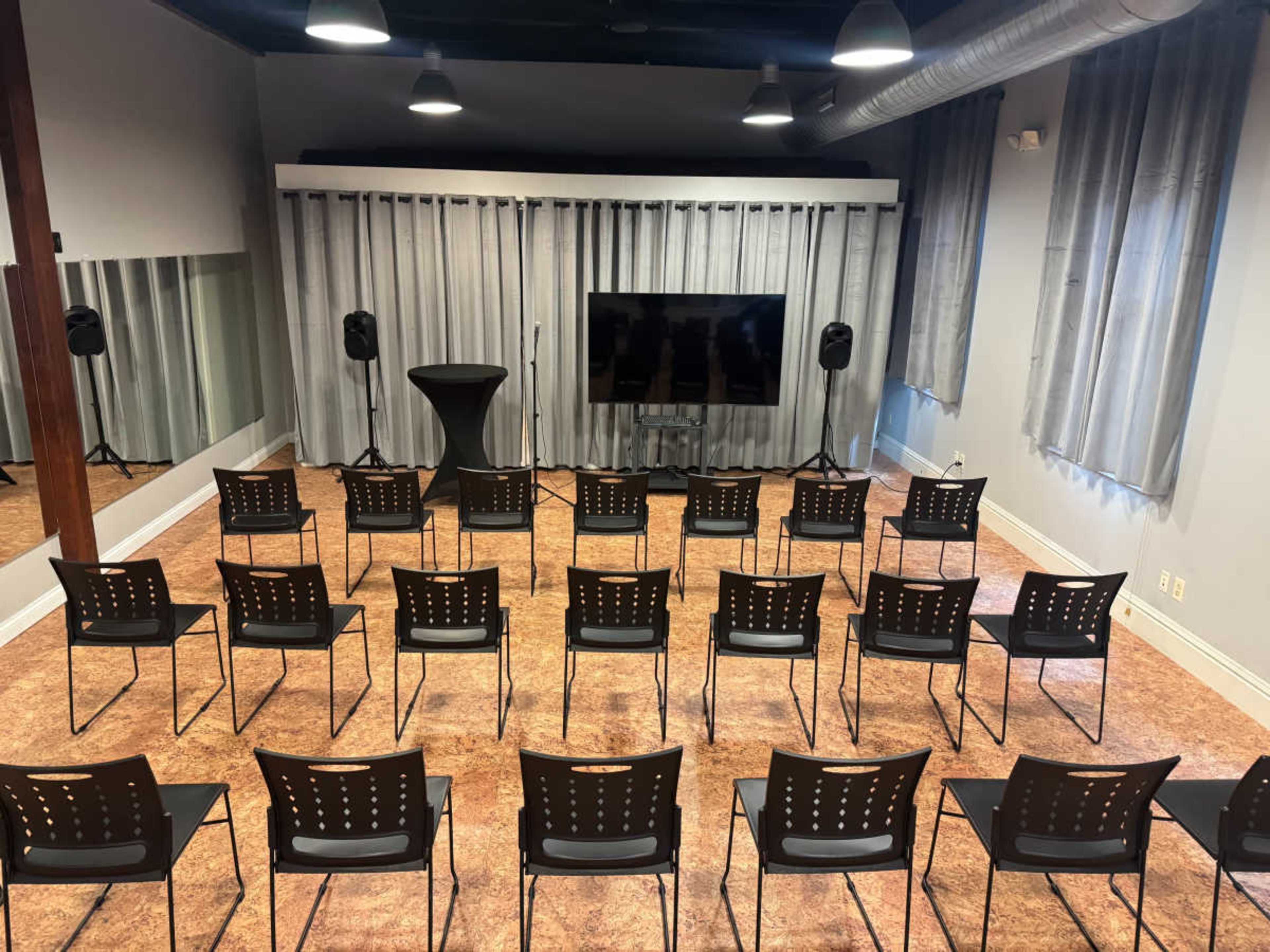 The image shows a room set up for a presentation or meeting, featuring rows of black chairs facing a television screen with a podium nearby.