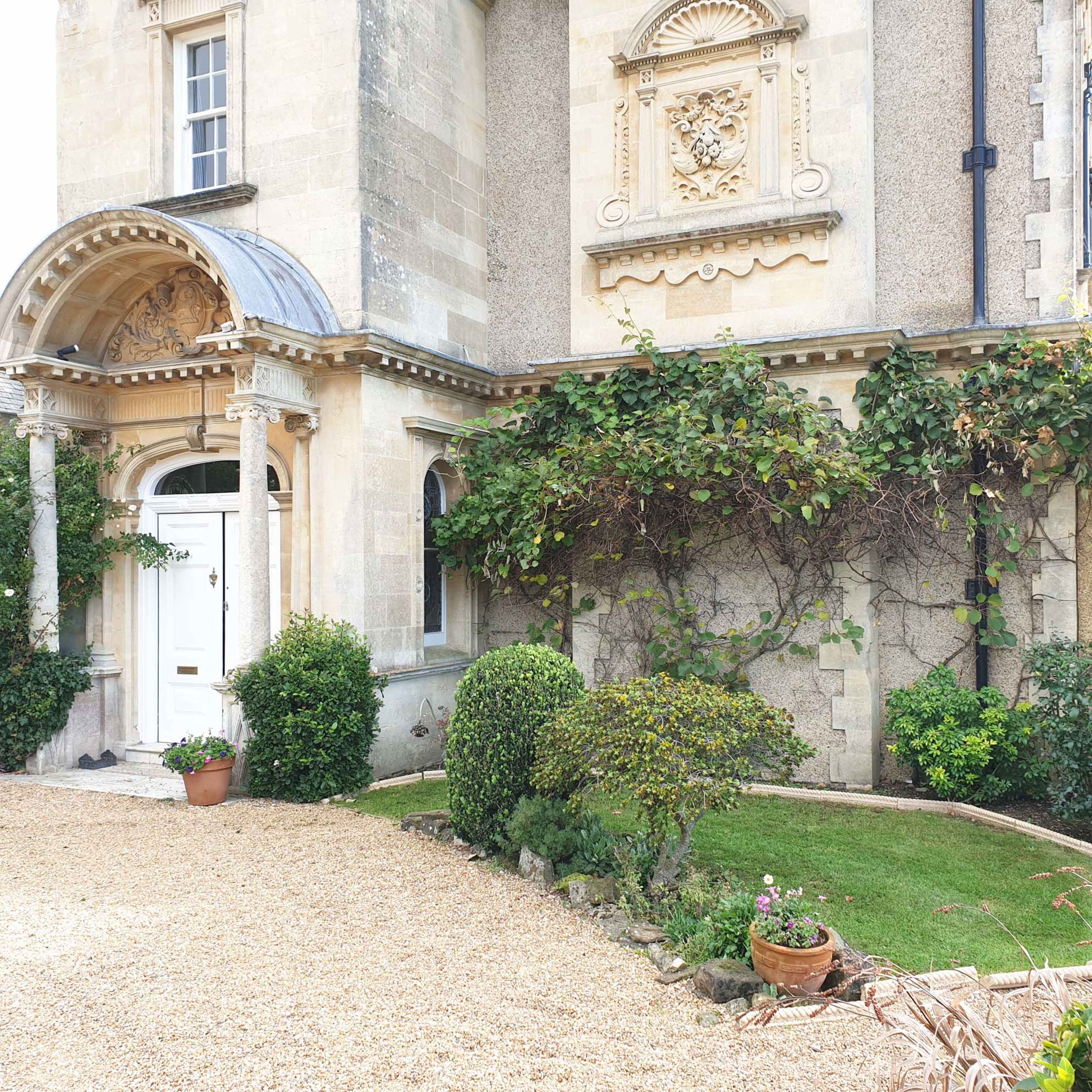 A stately building featuring intricate architectural details, surrounded by manicured shrubs and a gravel pathway.