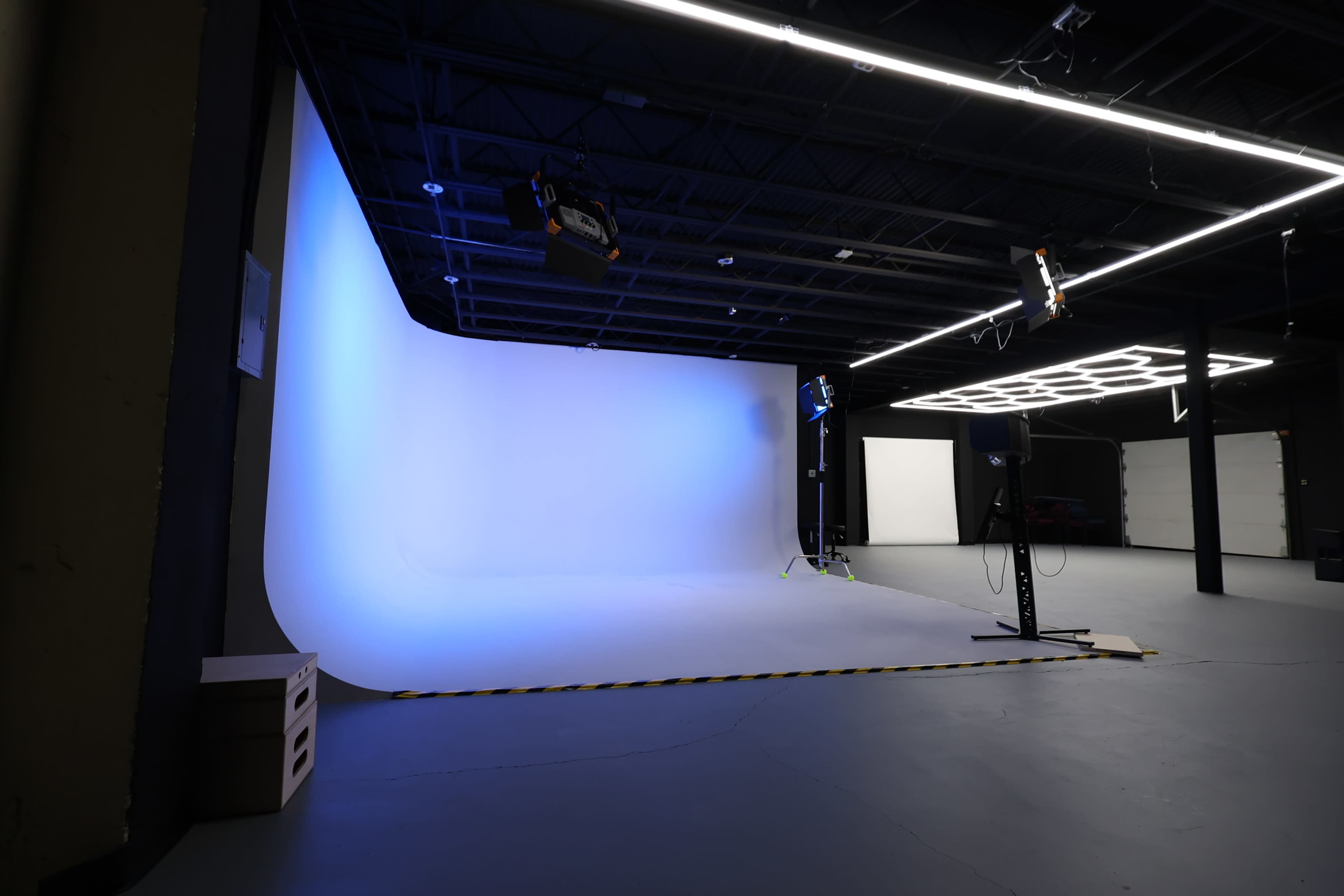 The image shows a spacious photography studio with a seamless blue backdrop and professional lighting equipment set up.