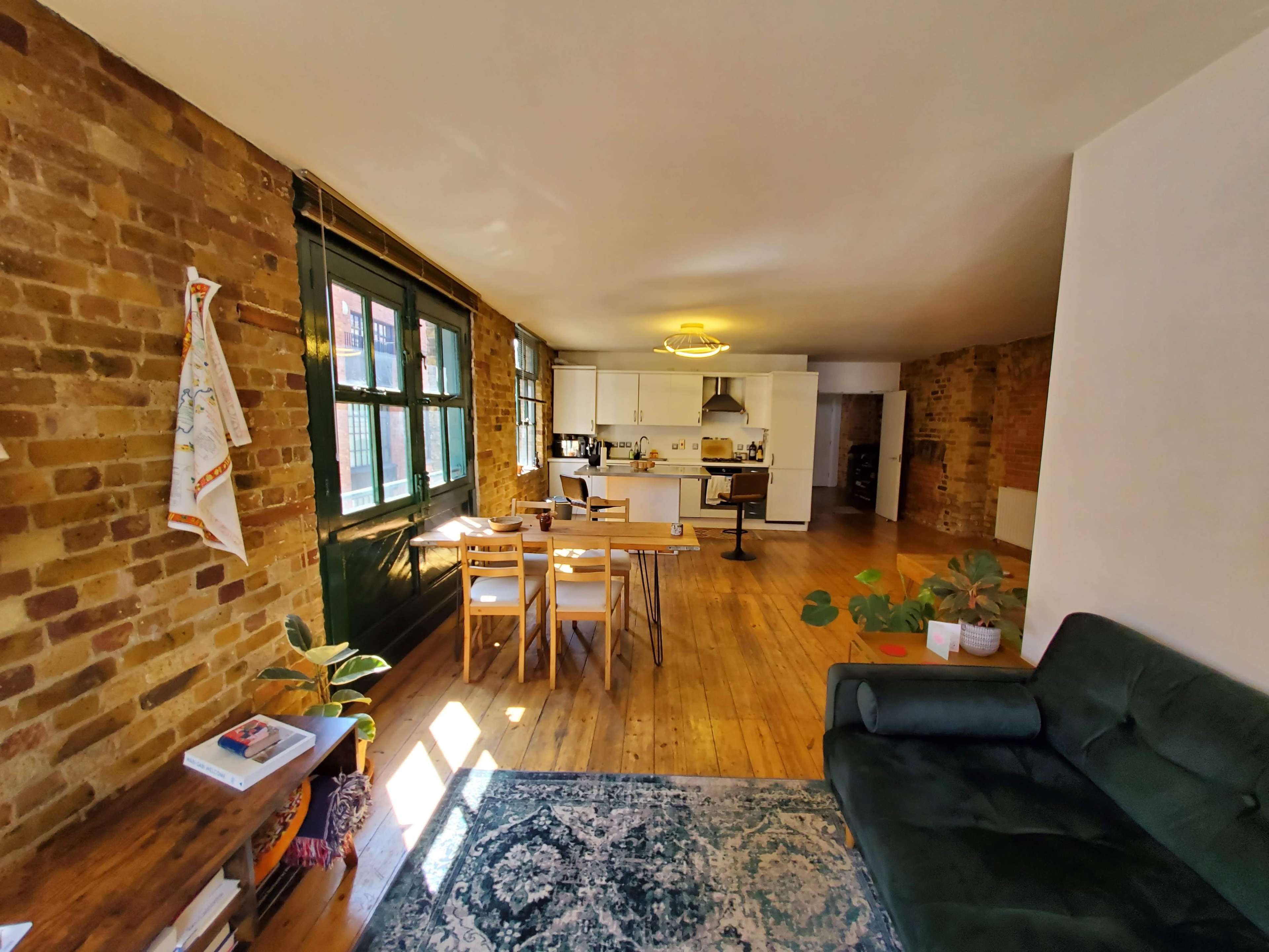 A spacious, open-concept living area featuring exposed brick walls, a dining table, and a kitchen at the far end.