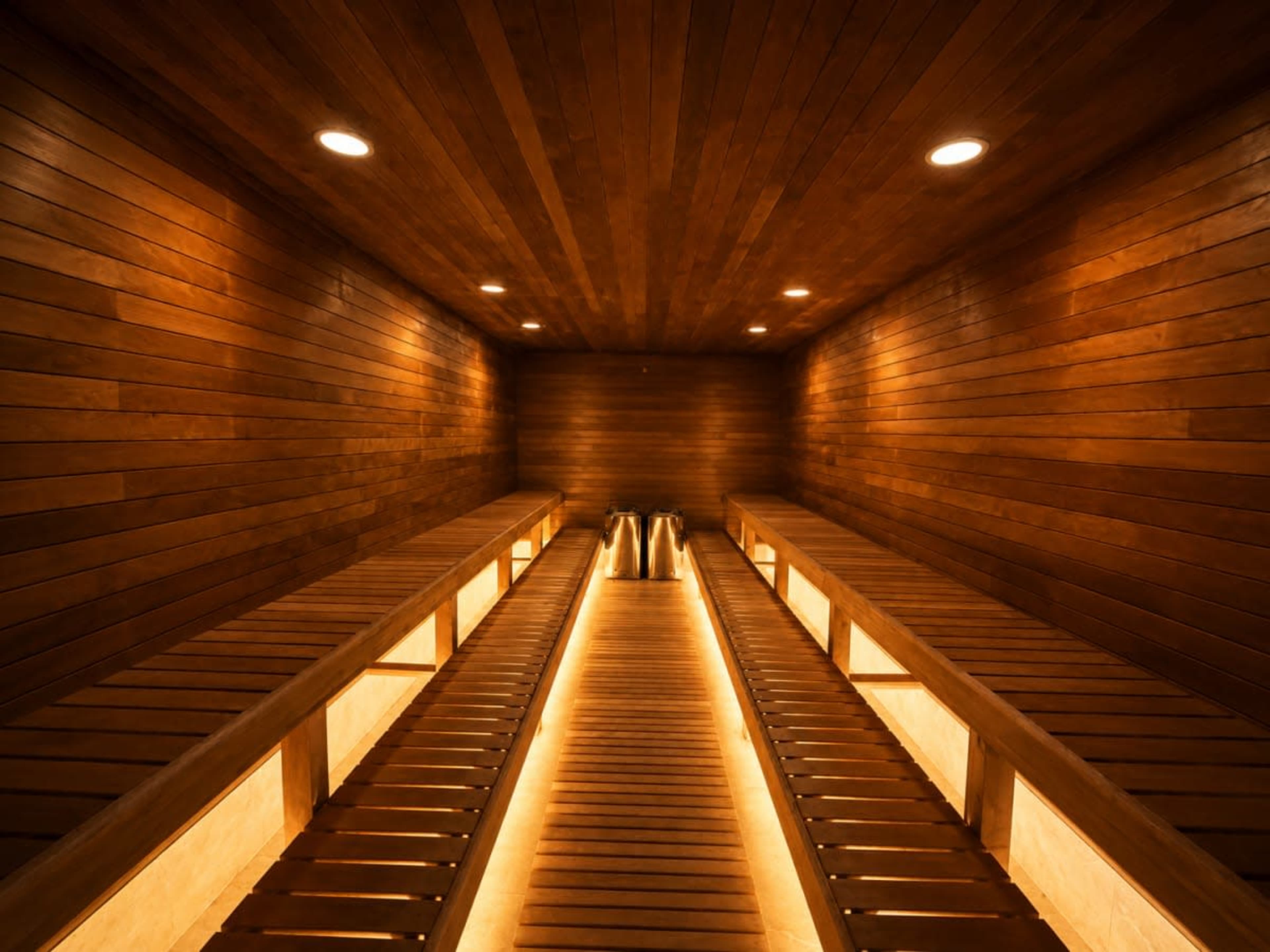 The image shows a wooden sauna interior with benches on either side and soft lighting creating a warm atmosphere.